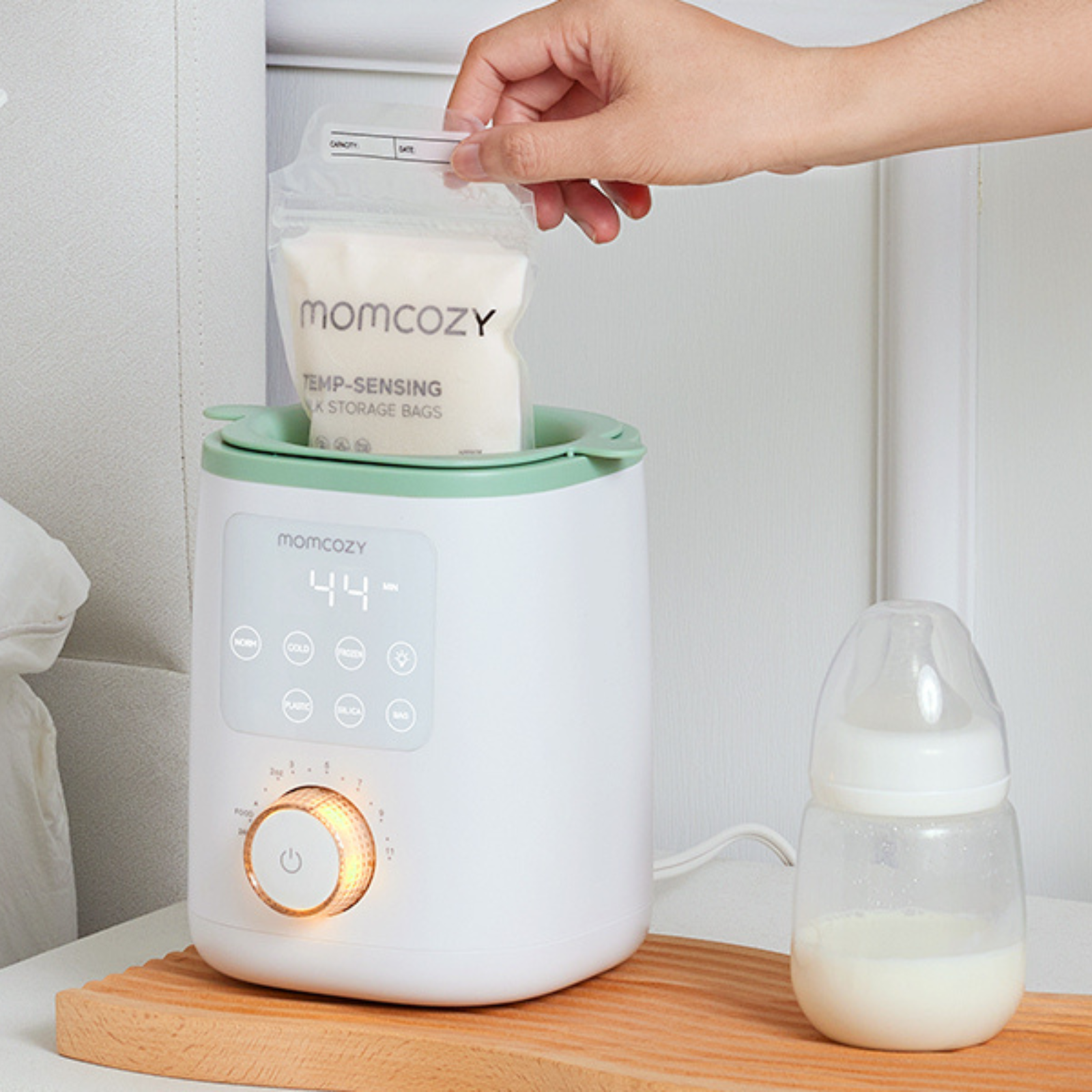 Une main place un sac de lait dans un chauffe-biberon blanc et vert.