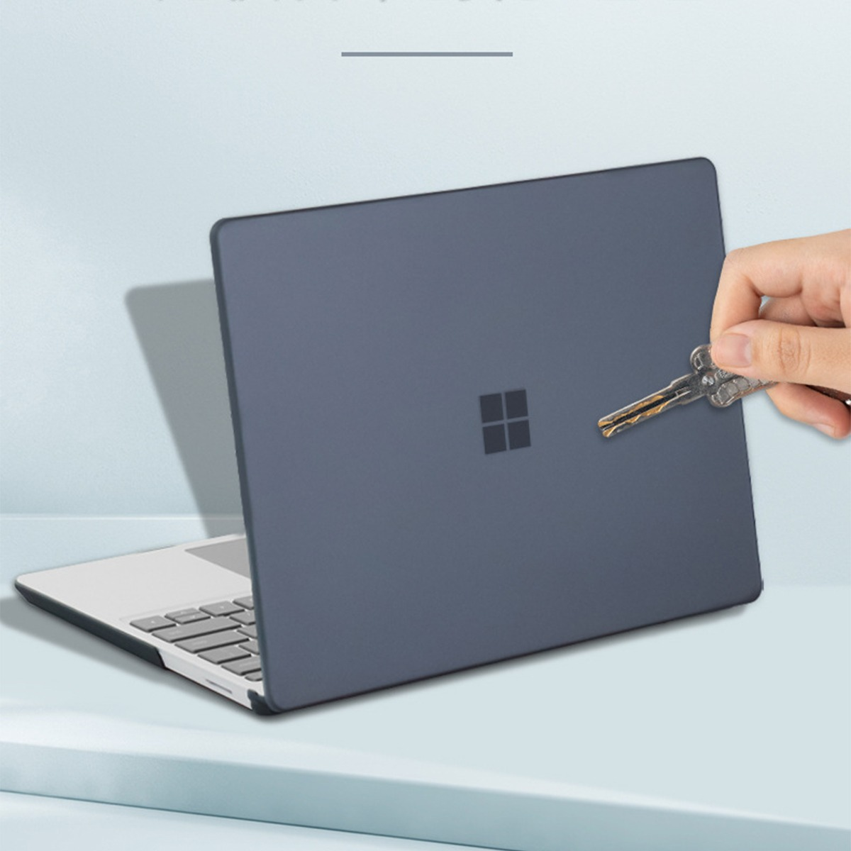 Dłoń trzyma klucz przed zamkniętym, ciemnym laptopem z logo Microsoft.