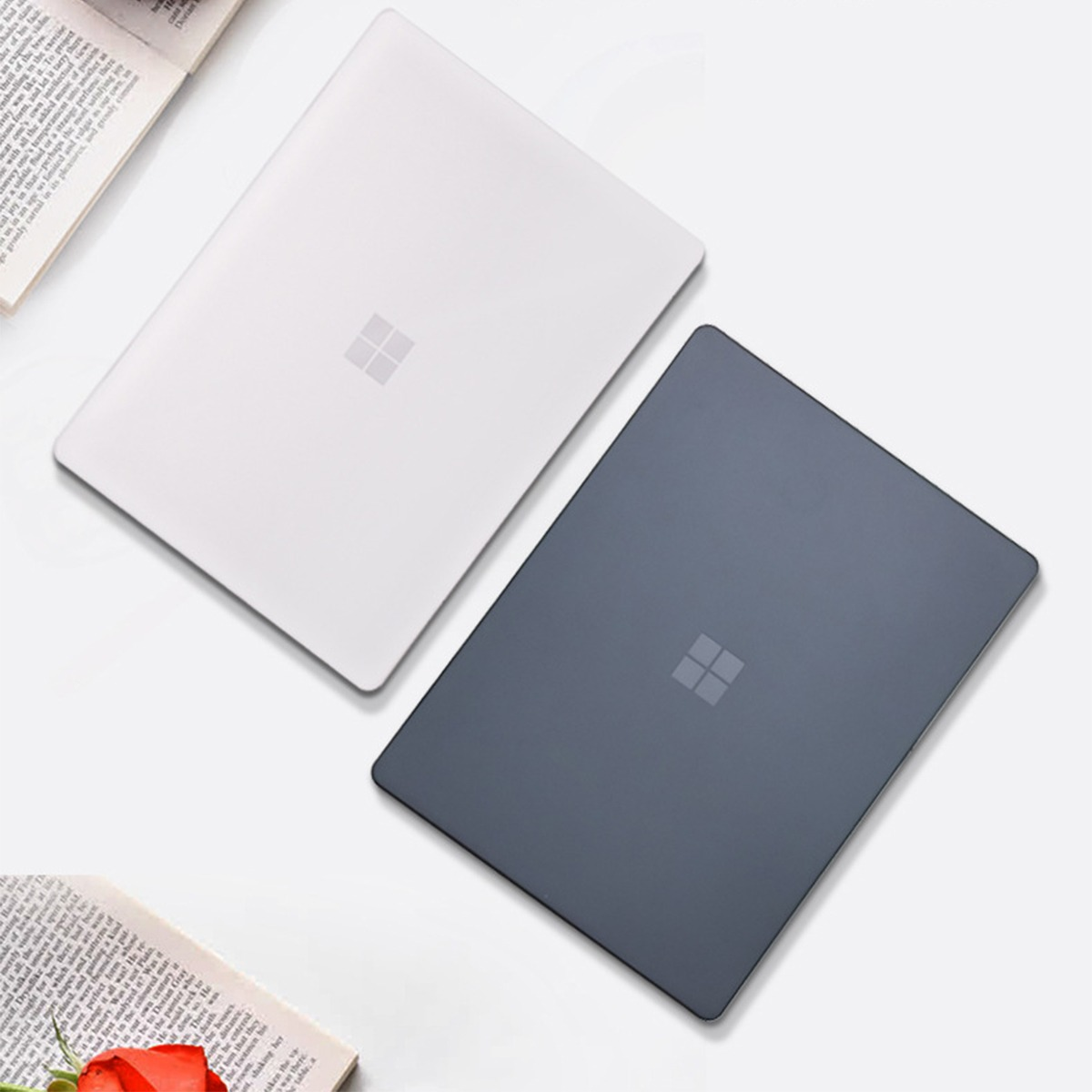 Dwa laptopy, jeden biały, drugi ciemnoszary, obok otwartej książki.