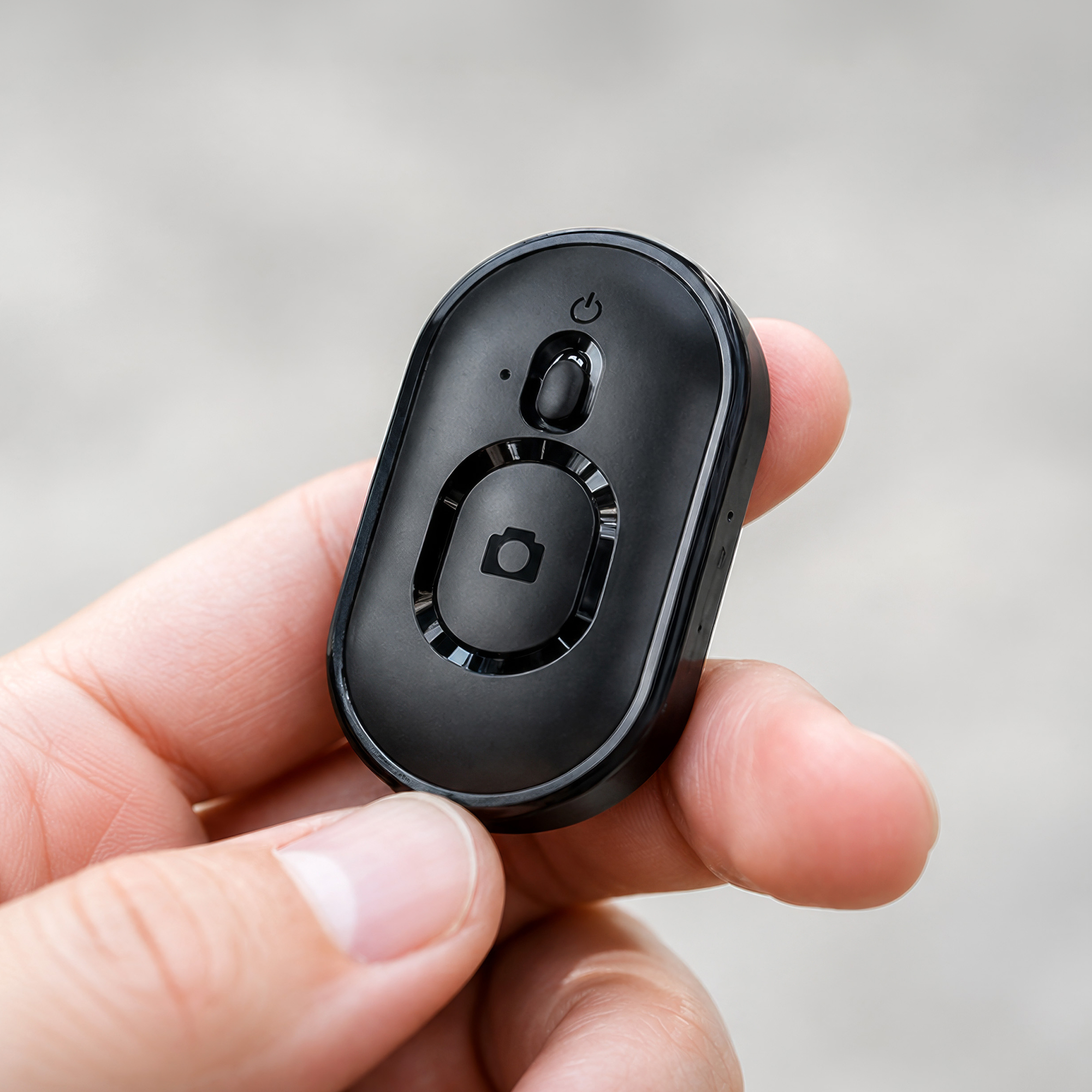 Czarny pilot Bluetooth z ikonami zasilania i aparatu, trzymany w dłoni.