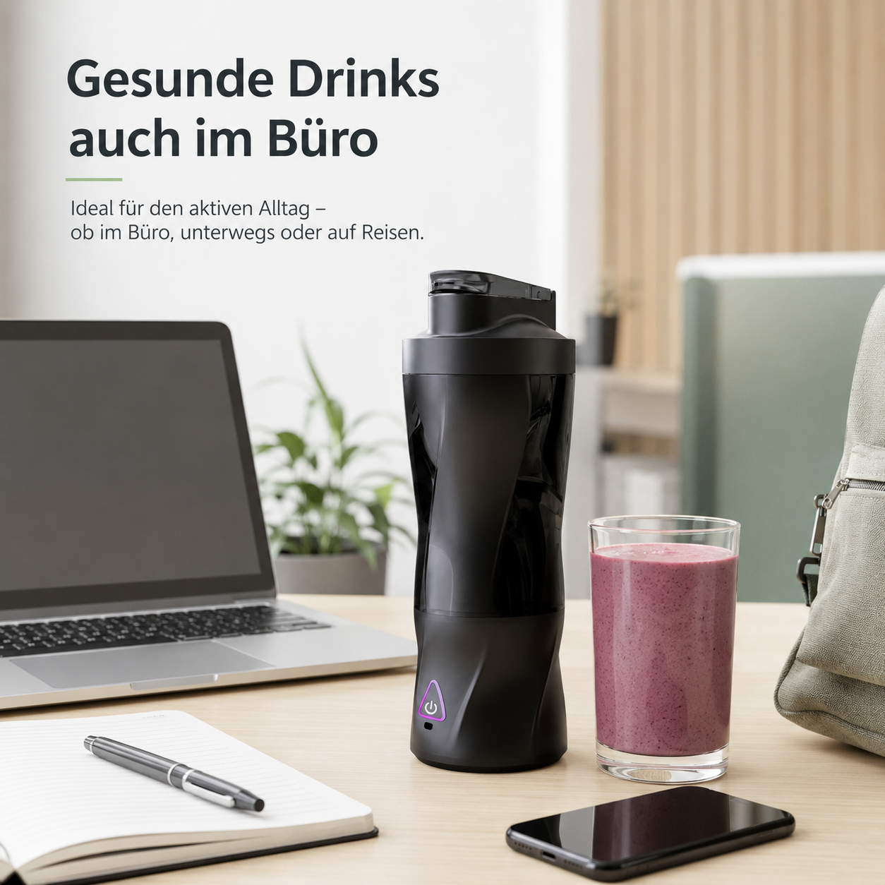 Schwarzer Mixer mit Smoothie, Laptop, Notizbuch und Handy auf einem Schreibtisch.