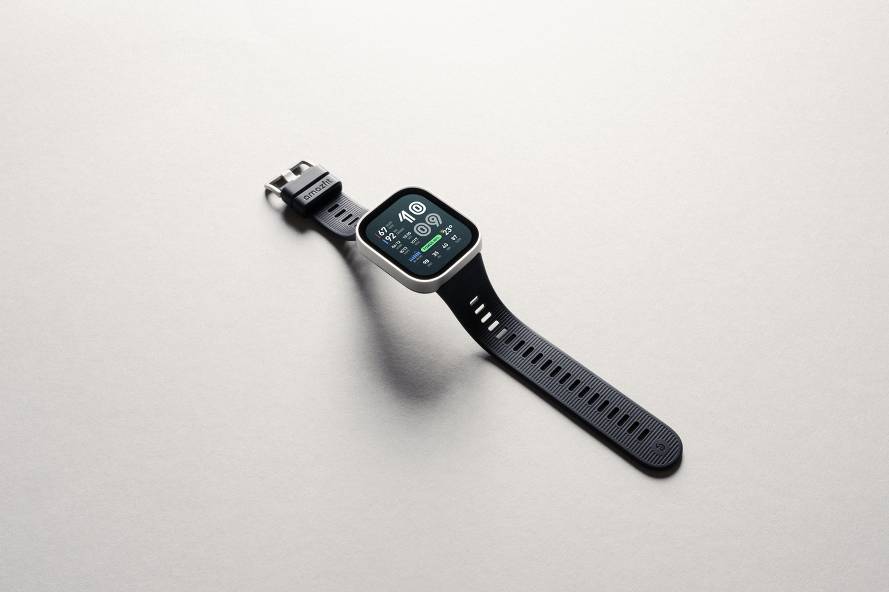 Un reloj Amazfit gris con correa oscura descansa sobre una superficie gris claro.