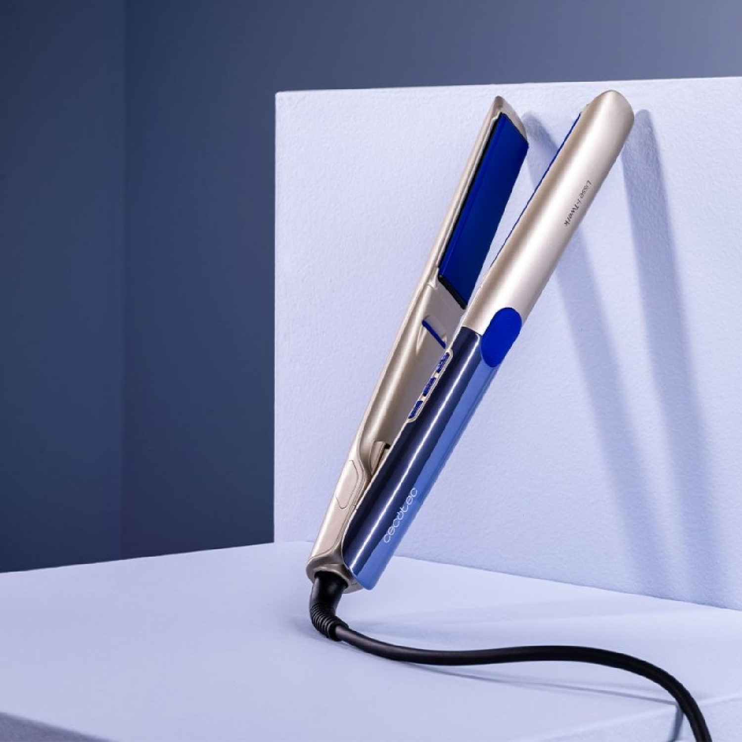 Plancha de pelo dorada y azul sobre superficie azul claro con fondo azul oscuro.
