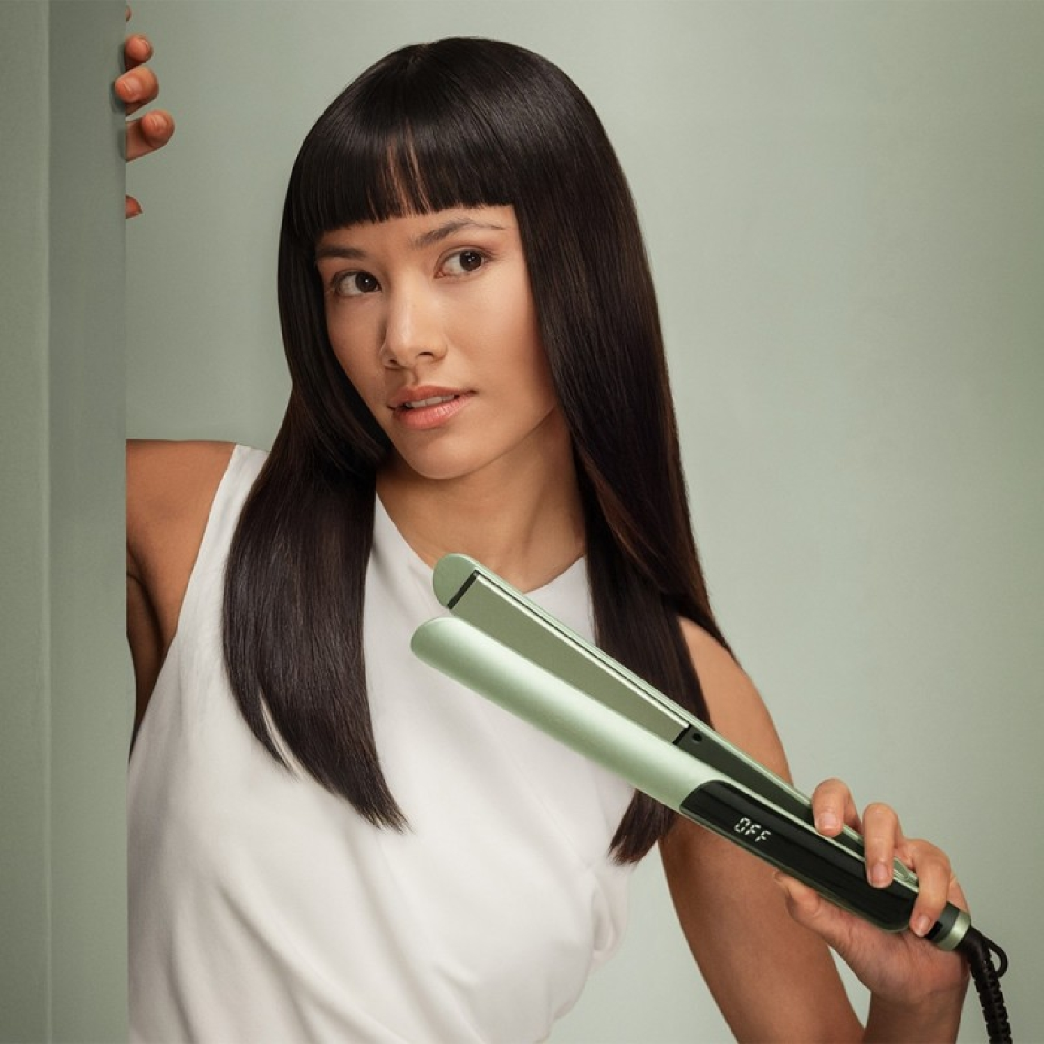 Una donna con lunghi capelli neri tiene una piastra per capelli verde chiaro con manico nero.