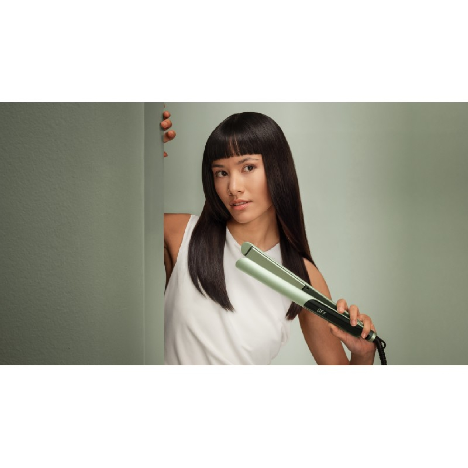 Una donna con lunghi capelli neri tiene una piastra per capelli verde chiaro.