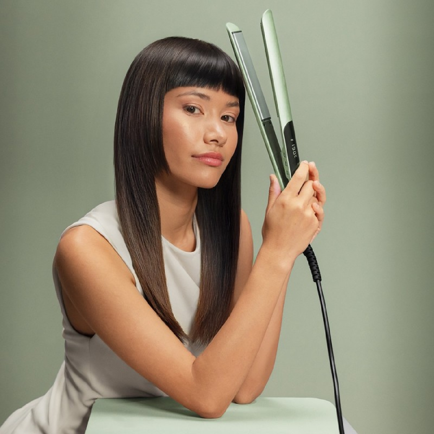 Donna con lunghi capelli scuri tiene una piastra verde chiaro su sfondo verde pallido.