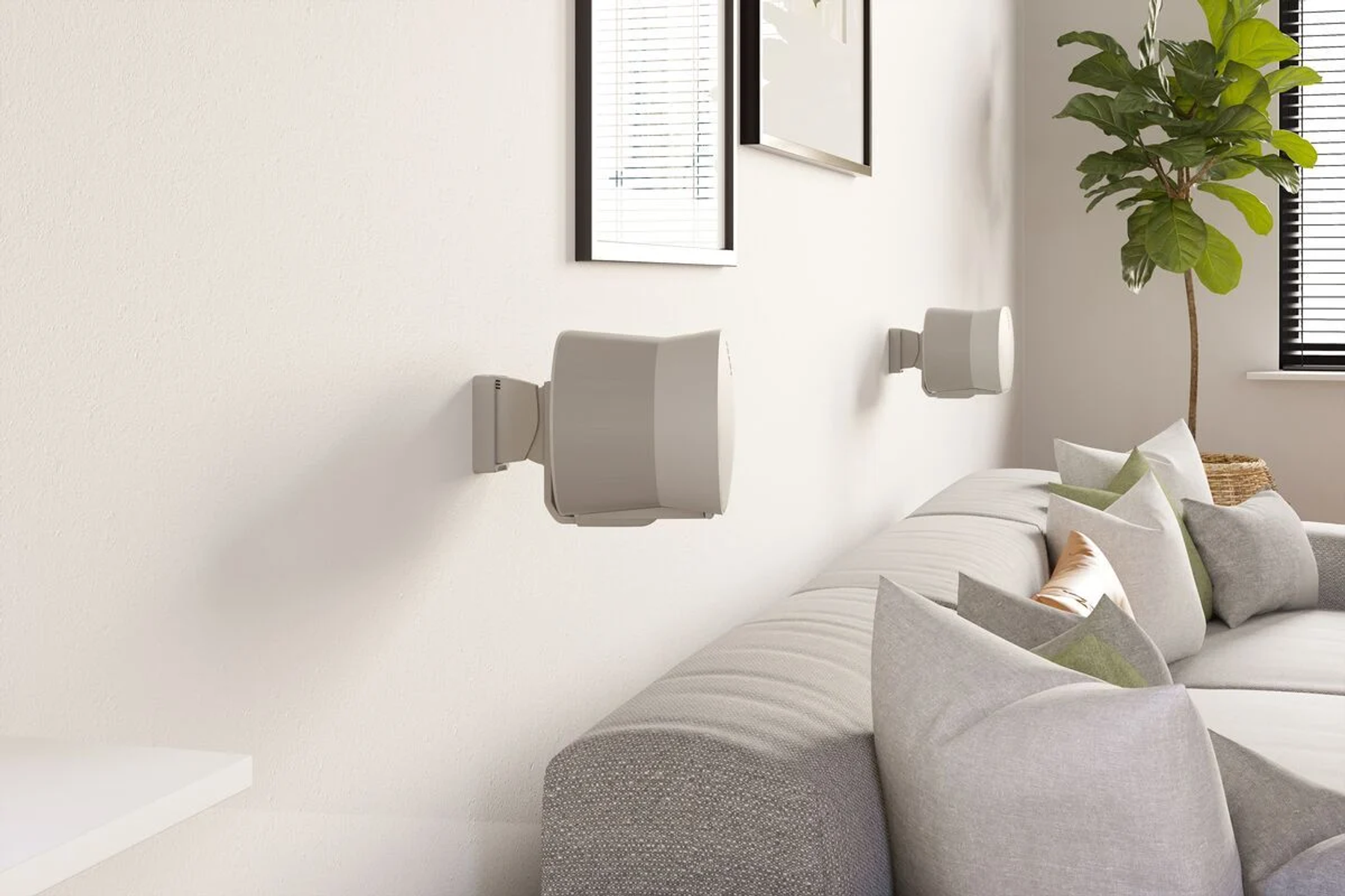 Graue Lautsprecher an einer weißen Wand über einem Sofa mit Kissen.