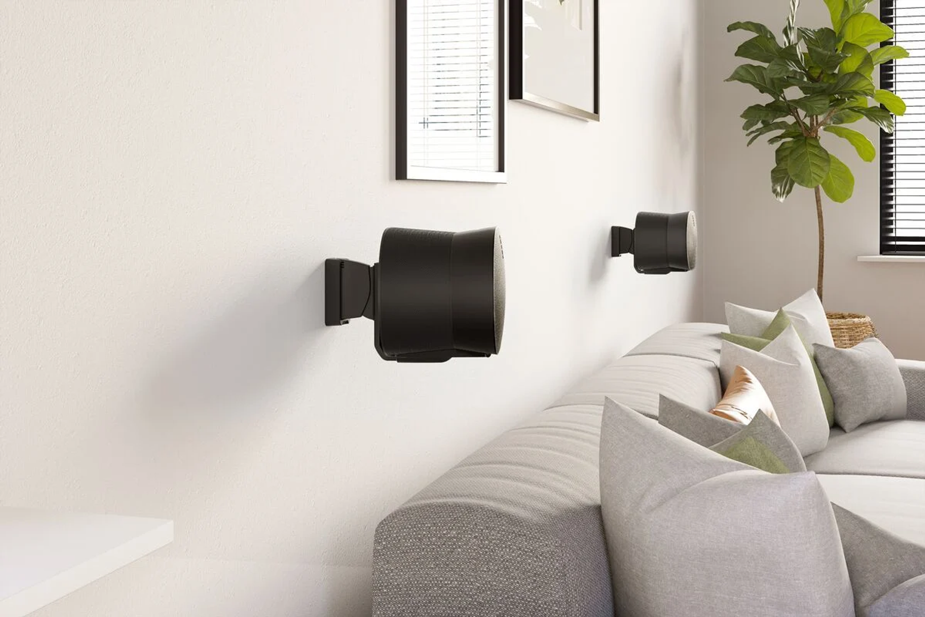 Zwei schwarze Wandlautsprecher befinden sich in einem modernen Wohnzimmer mit Sofa.