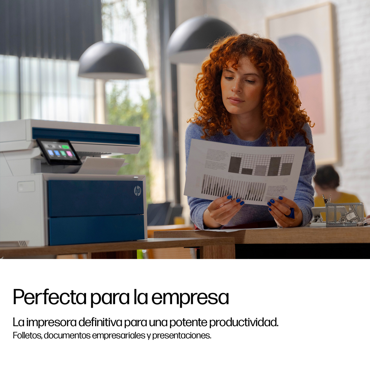 Una donna con capelli rossi ricci esamina un documento accanto a una stampante HP blu e bianca.