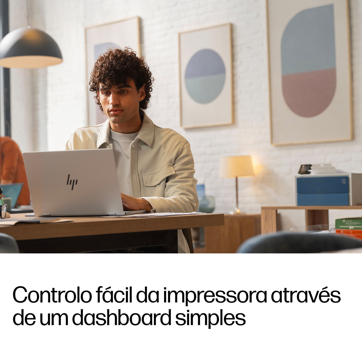 Uomo con capelli ricci lavora su un laptop in un ufficio luminoso con opere d'arte.