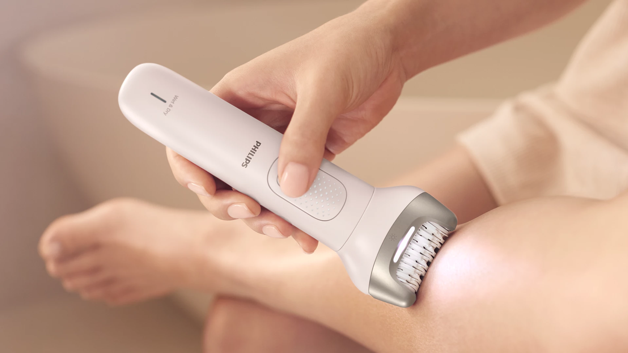 Una mano tiene un epilatore Philips bianco usato su una gamba.