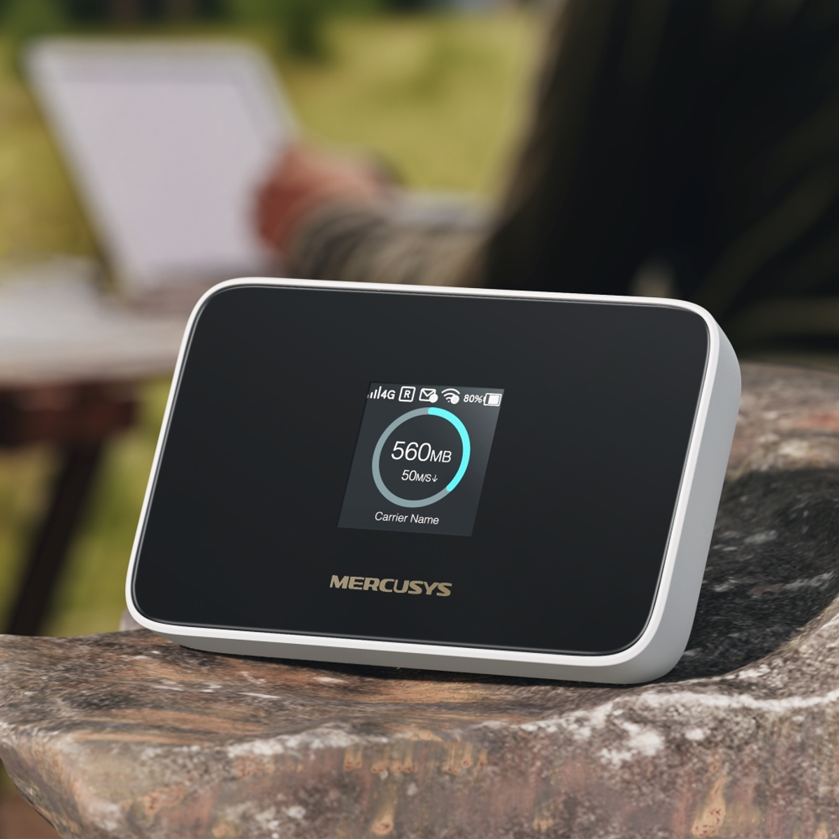 Un hotspot Wi-Fi MERCUSYS su una pietra con un laptop sfocato sullo sfondo.