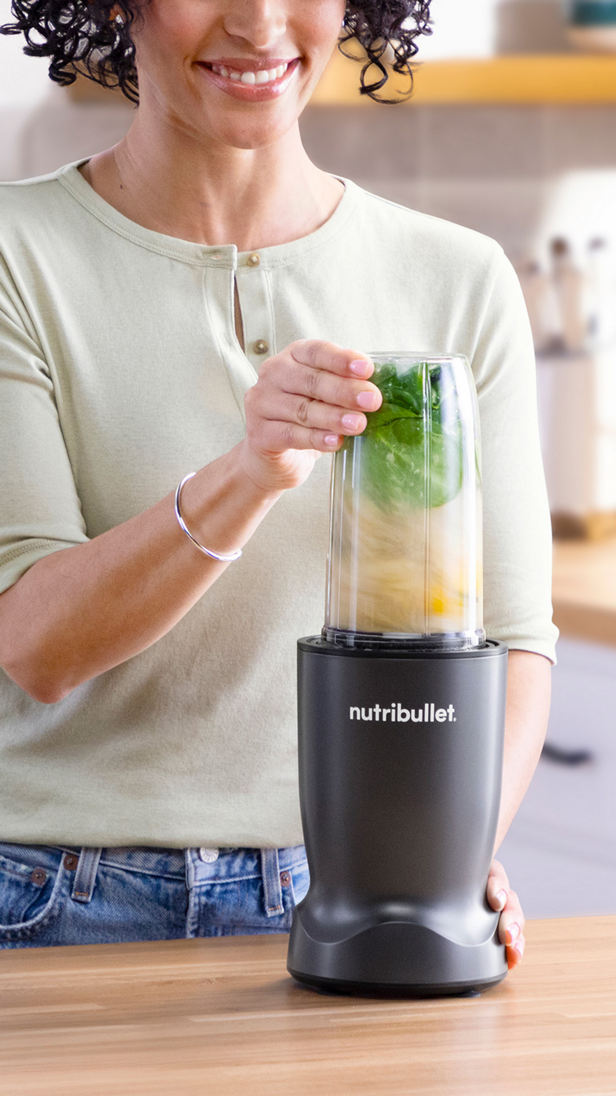 Eine Frau mixt grüne Blätter und Obst in einem Nutribullet-Mixer.