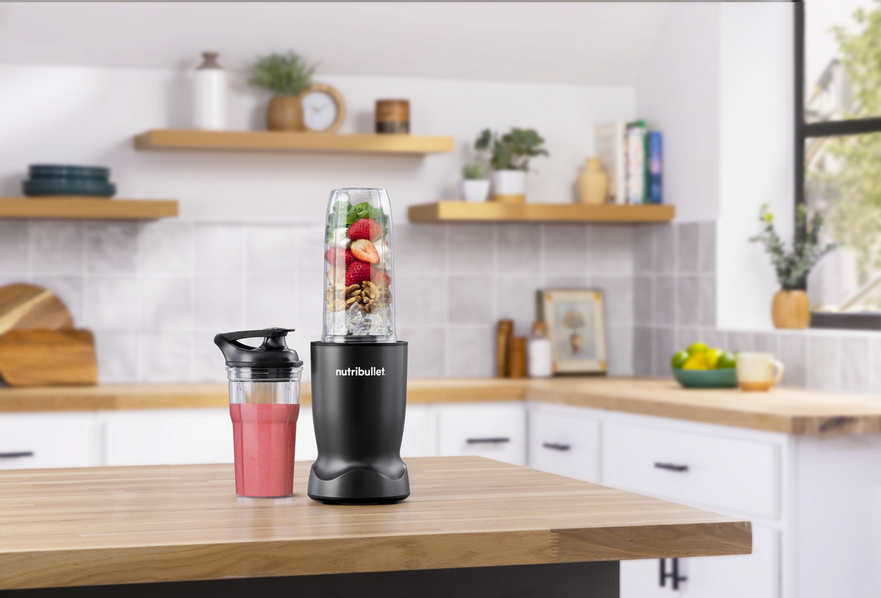 Ein schwarzer Nutribullet Mixer mit Beeren und Nüssen, daneben ein Becher mit Smoothie.