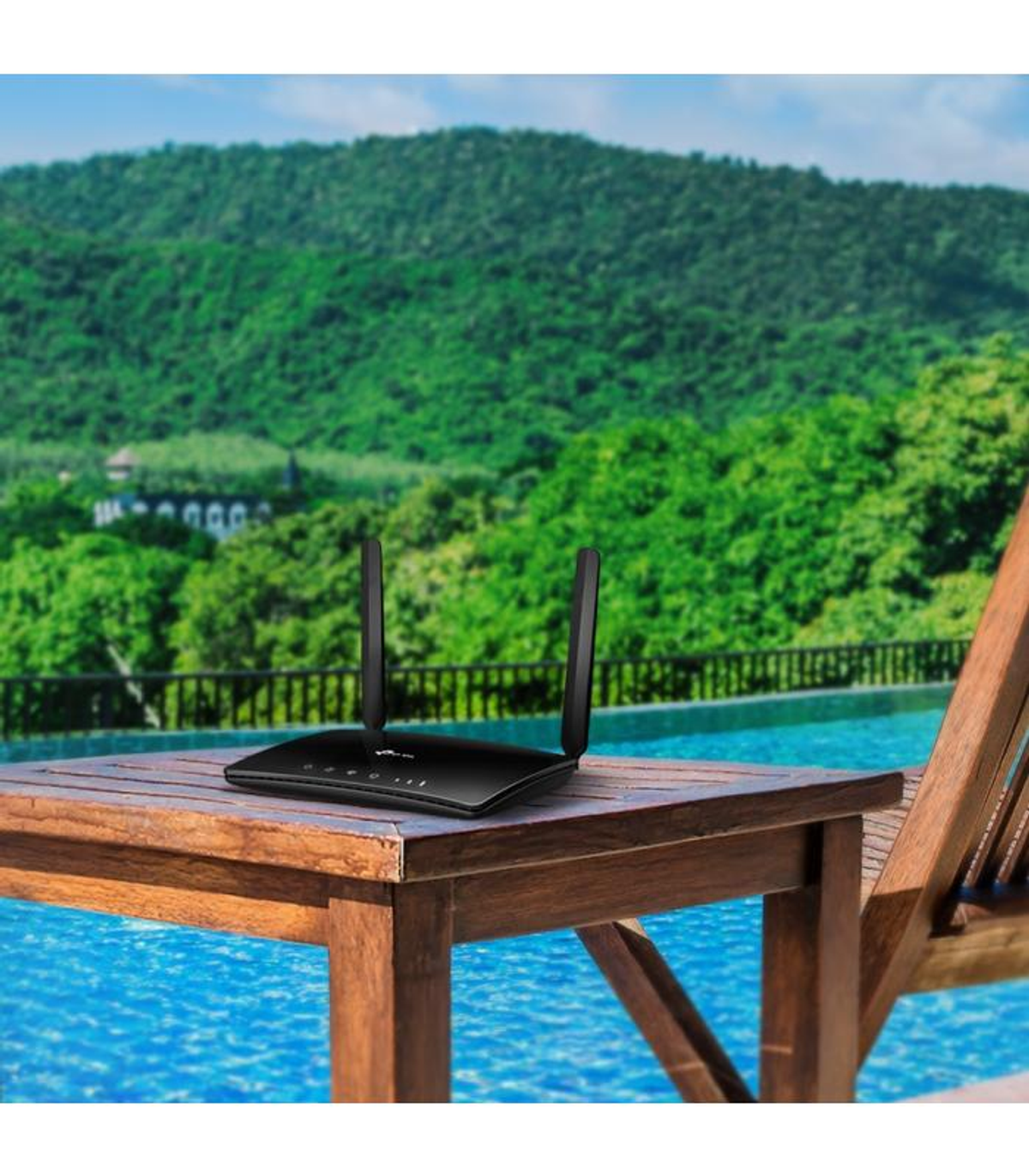 Router negro con antenas en mesa de madera junto a piscina, montañas al fondo.