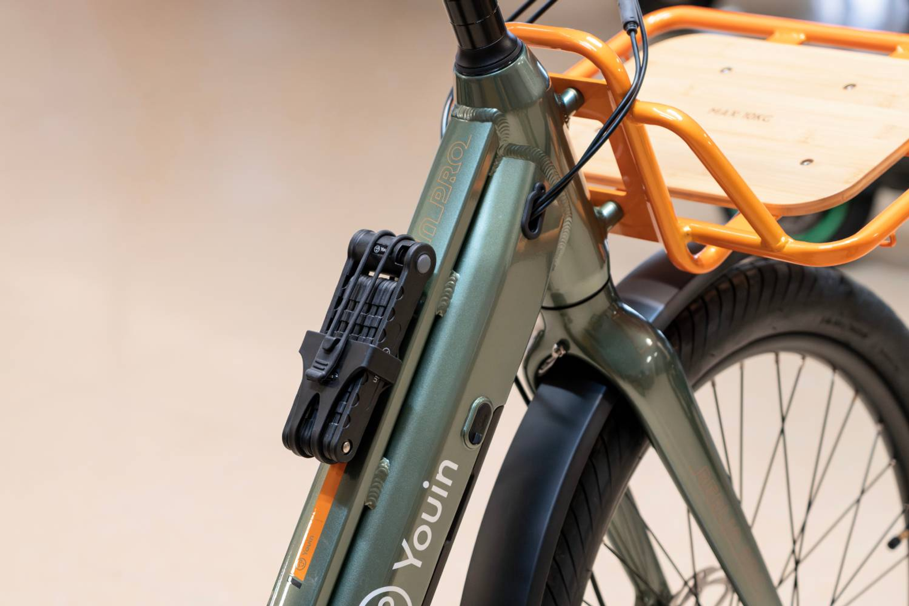 Bicicleta verde con candado plegable negro en el cuadro y portaequipajes naranja.