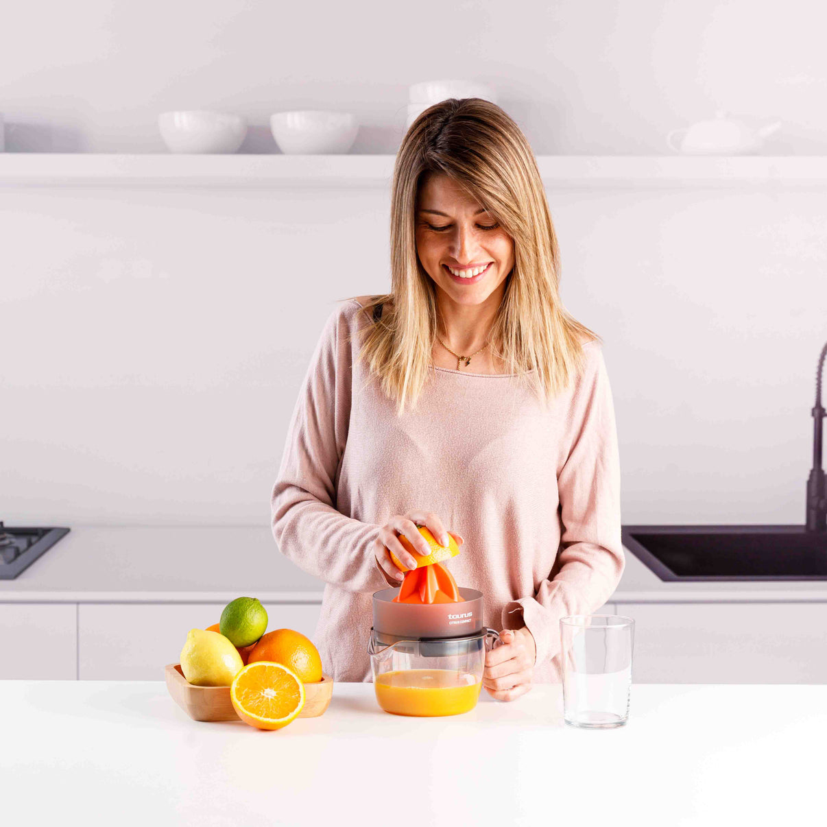Mujer exprimiendo limón en exprimidor con frutas y vaso cerca.