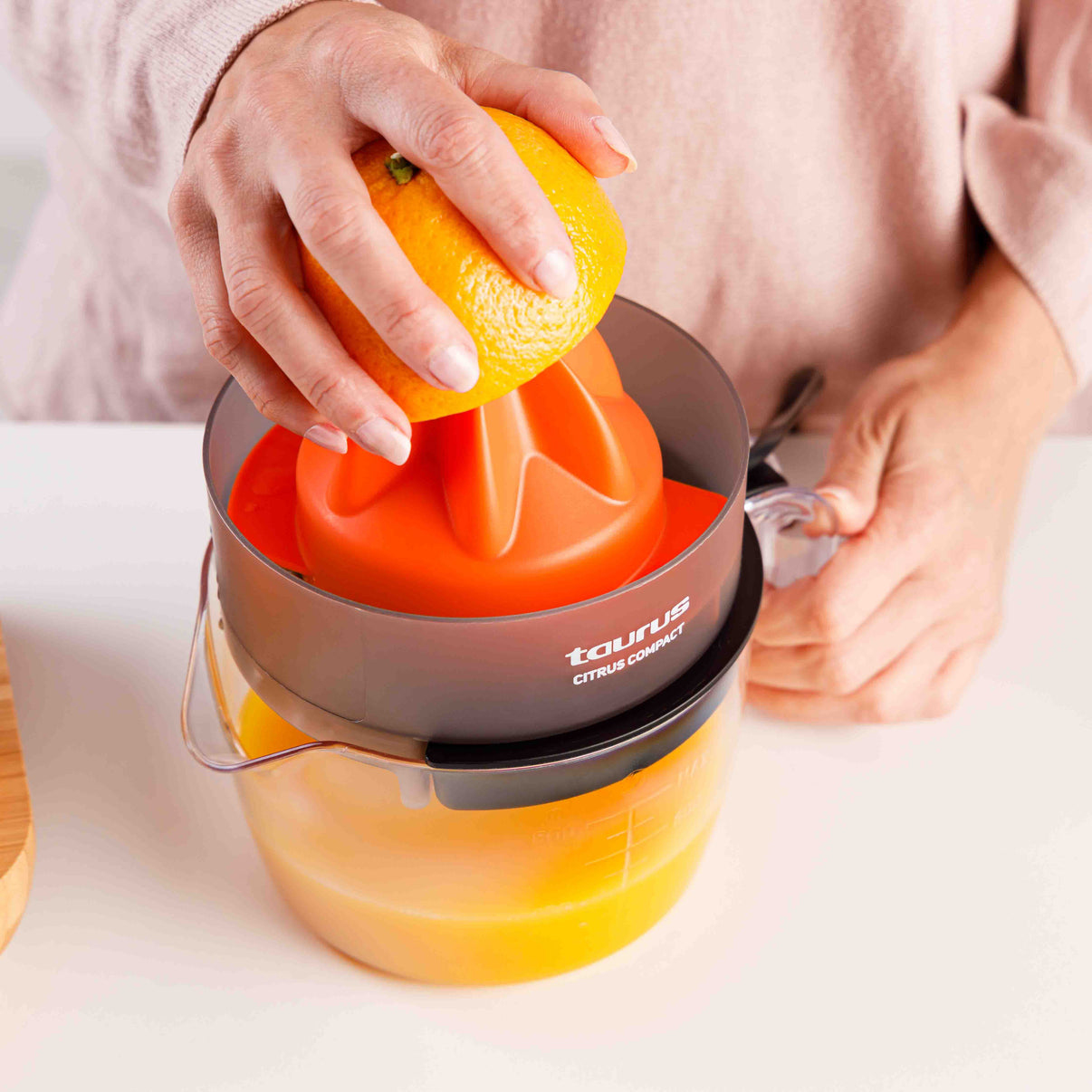 Naranja siendo presionada en exprimidor, jugo en recipiente.
