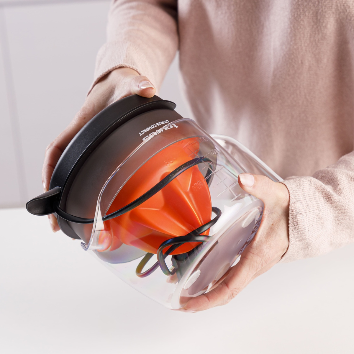 Una persona sujeta un accesorio exprimidor de cítricos naranja en una taza medidora.