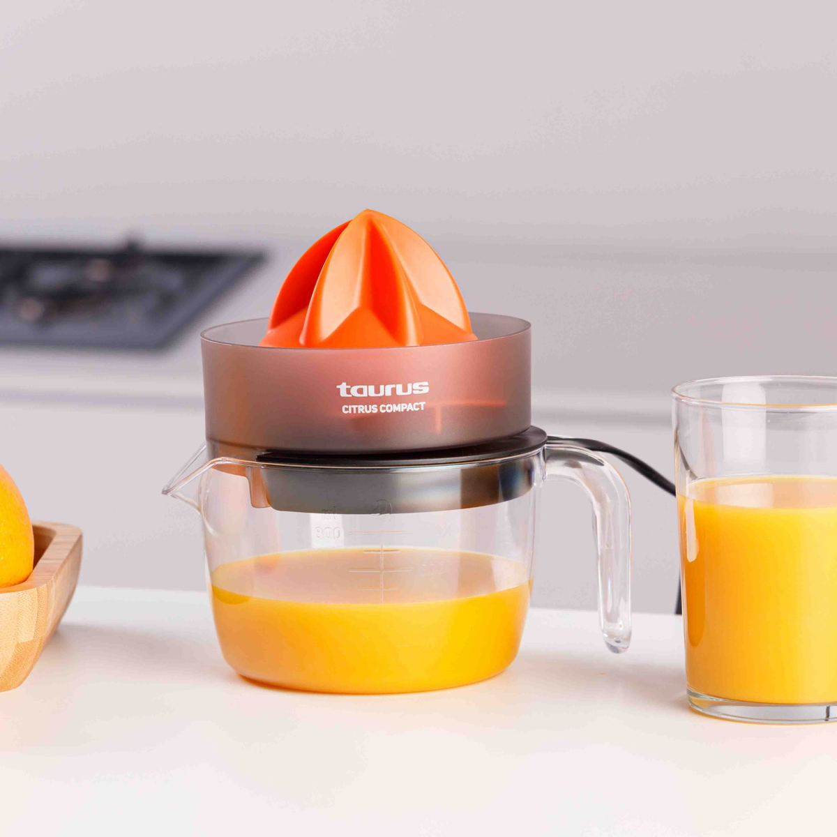 Un exprimidor de cítricos naranja con un vaso medidor lleno de zumo y un vaso de zumo al lado.