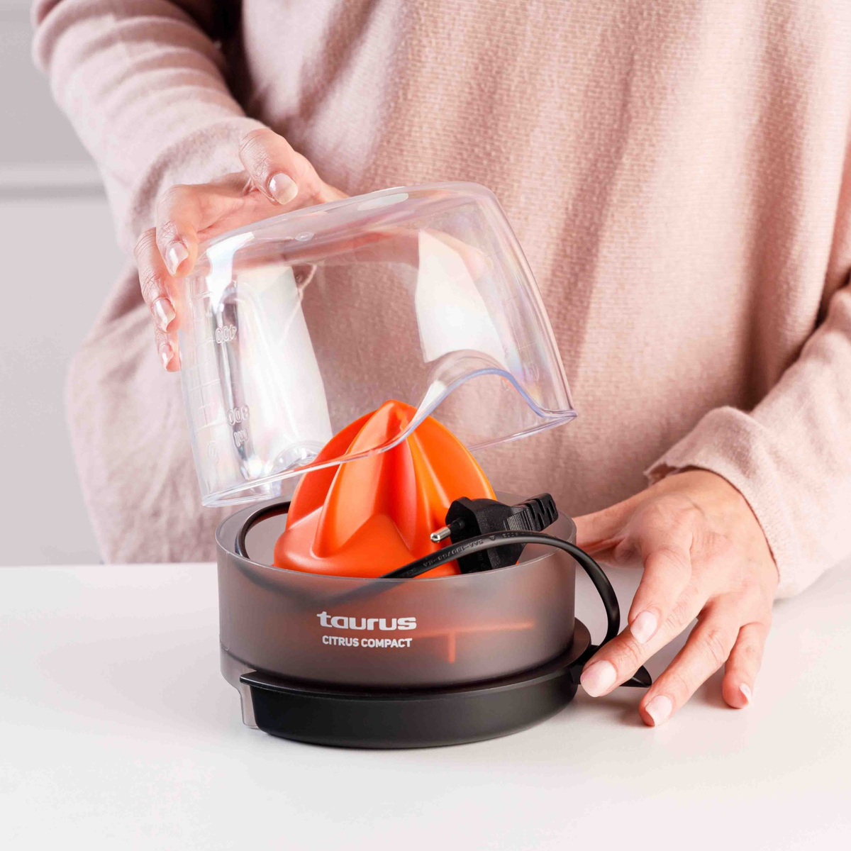 Una persona sujeta la tapa de un exprimidor de cítricos naranja. El recipiente es transparente.