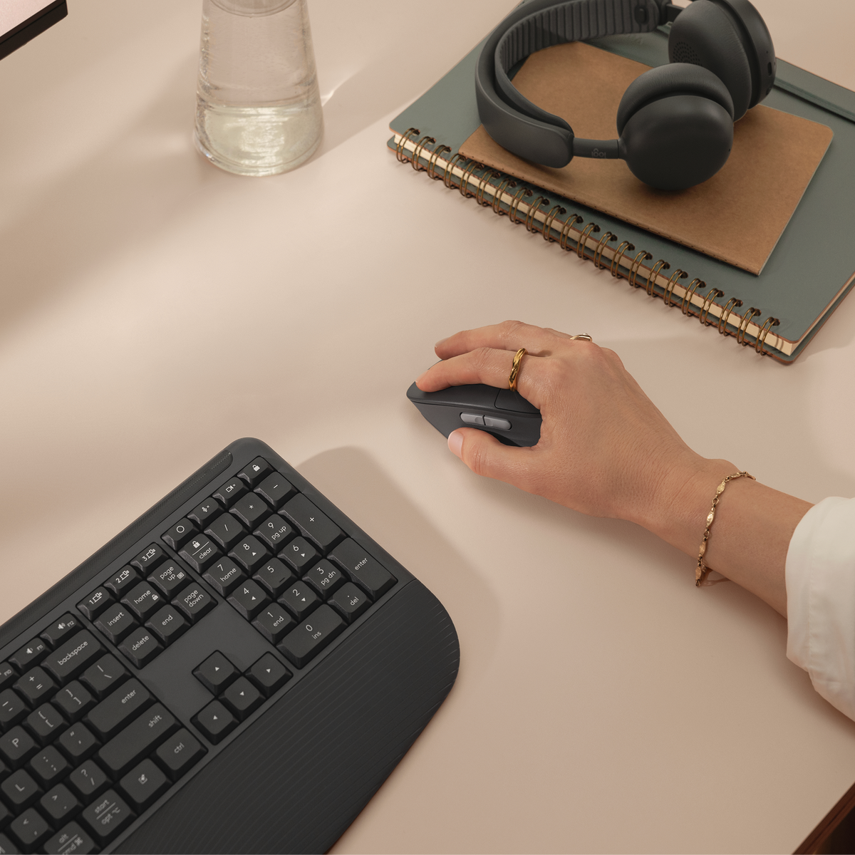 Una mano usa un mouse per computer grigio scuro su una scrivania beige accanto a una tastiera.