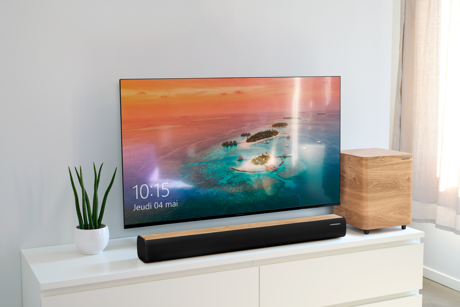 Un televisor de pantalla plana muestra una isla tropical. A su lado hay un subwoofer y una barra de sonido.