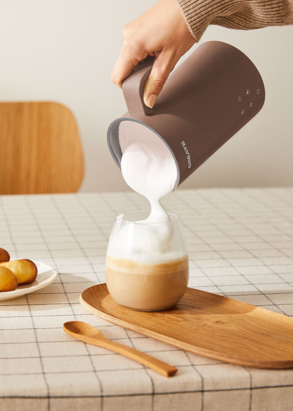 Jarra marrón vertiendo espuma de leche en un vaso de latte macchiato.