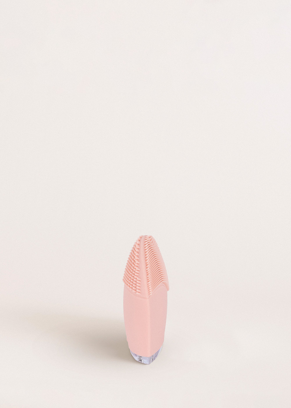 Un cepillo limpiador facial rosa con cerdas de silicona sobre fondo claro.