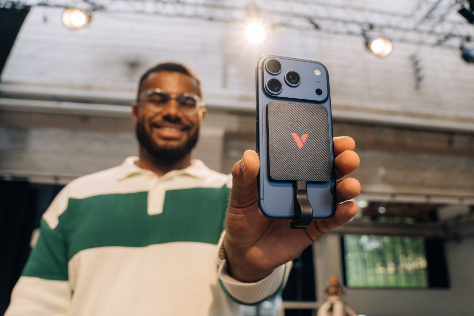 Ein Mann mit Brille hält ein blaues iPhone mit einer schwarzen Ladehülle und rotem Logo.