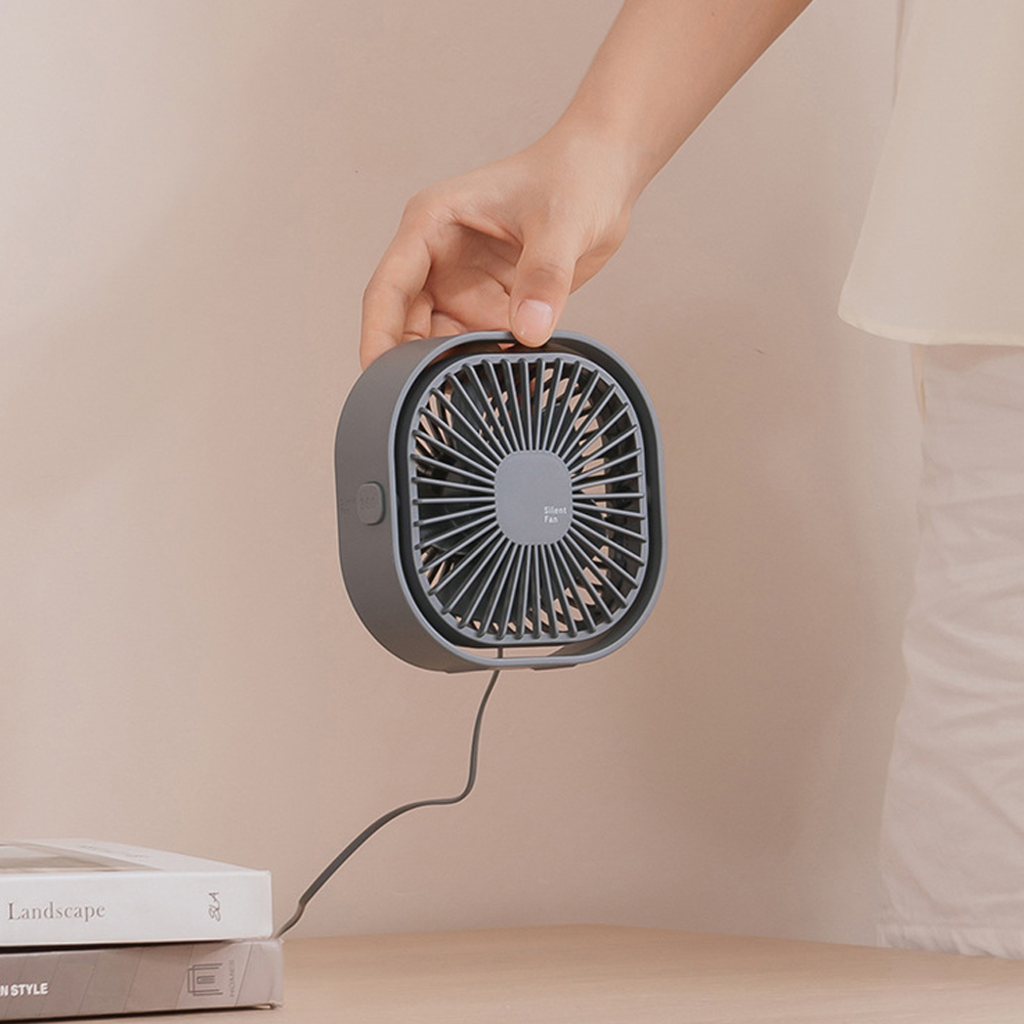 Eine Hand hält einen kleinen grauen Ventilator über gestapelten Büchern.