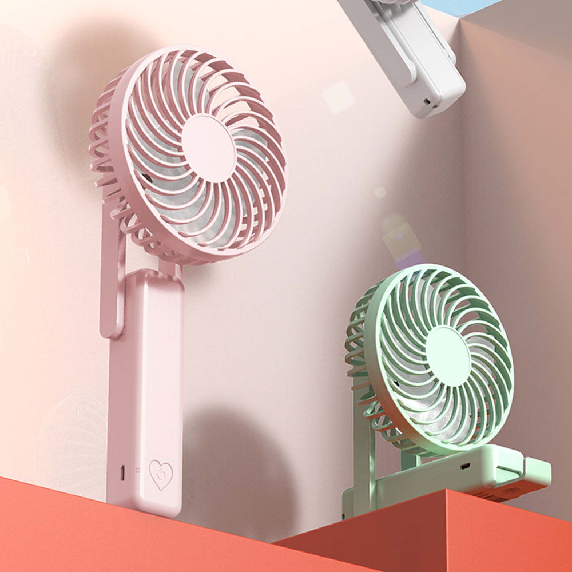 Zwei tragbare Ventilatoren, rosa und mintgrün, stehen auf orangen Würfeln.