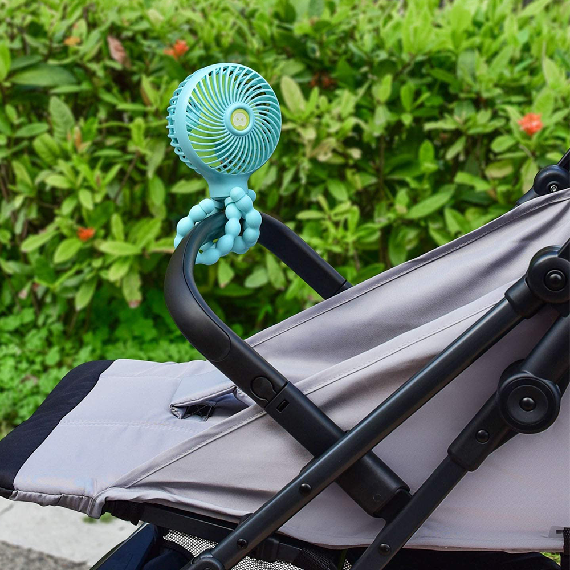 Ein blauer Babyventilator mit flexiblen Beinen, der am Griff eines Kinderwagens befestigt ist.