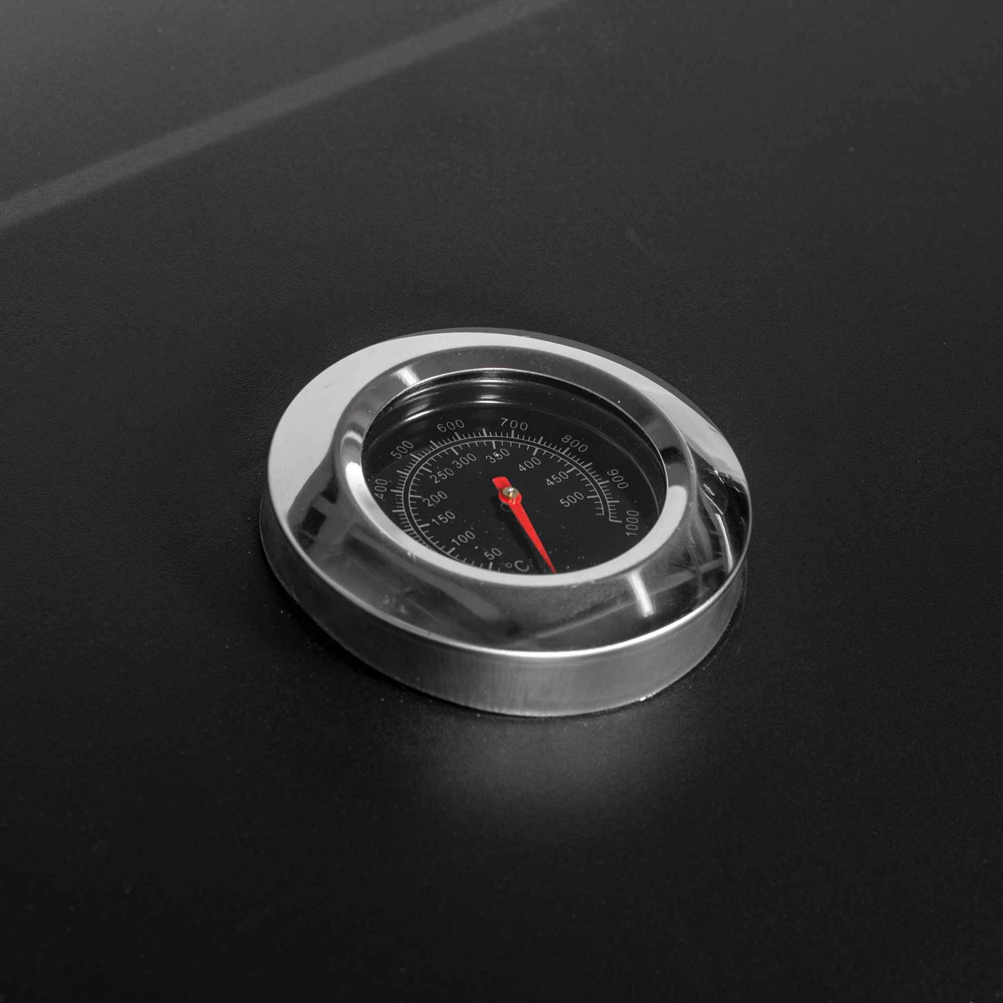 Ein Thermometer mit rotem Zeiger auf schwarzem Zifferblatt, Skala bis 1000°C.