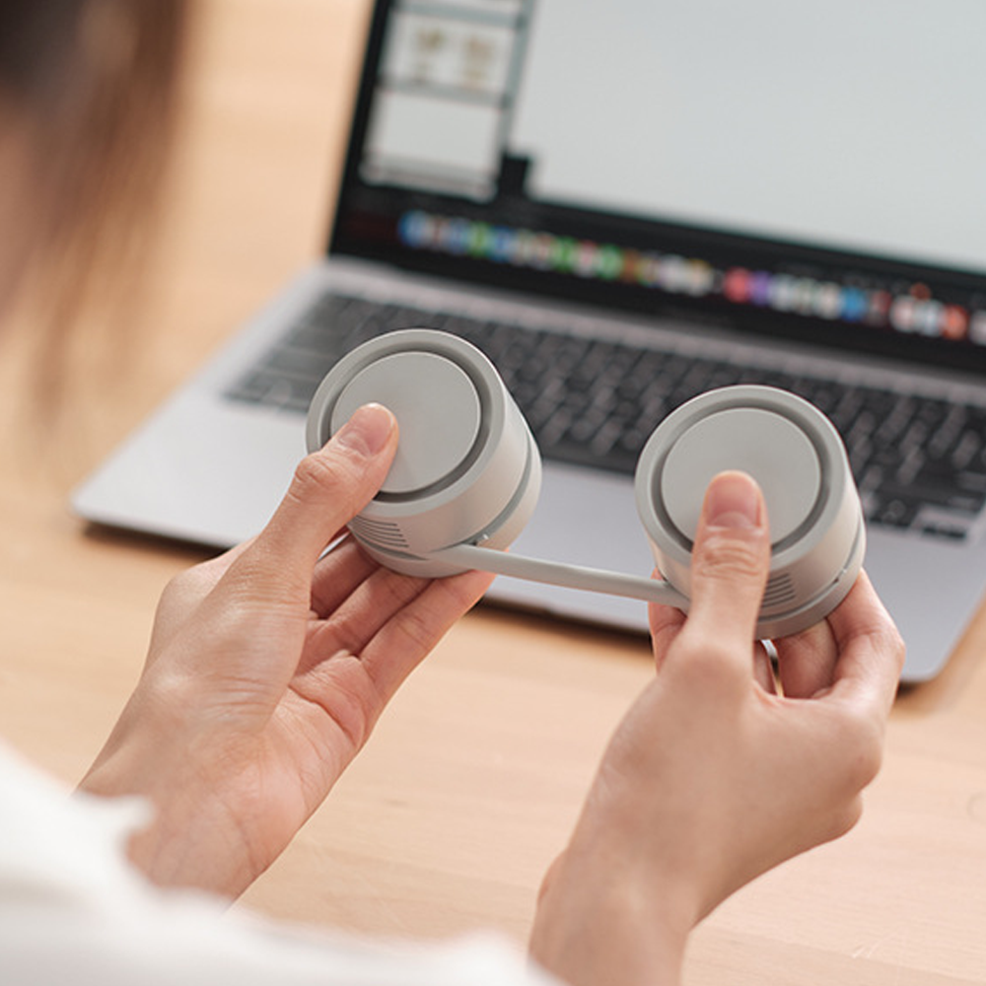 Grauer Nackenventilator wird von Händen vor einem Laptop gehalten.
