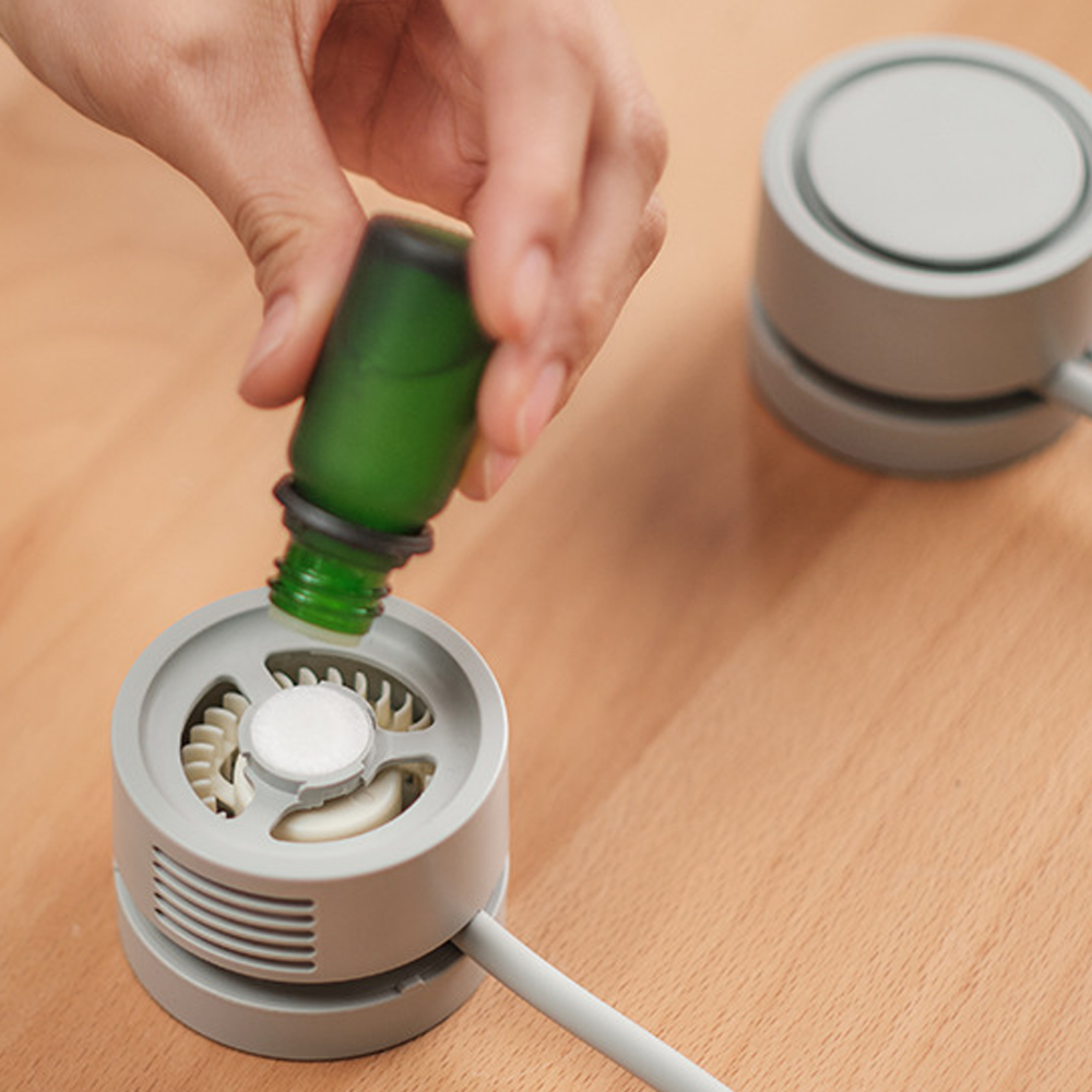 Eine Hand tropft Öl aus einer grünen Flasche in einen Diffusor.
