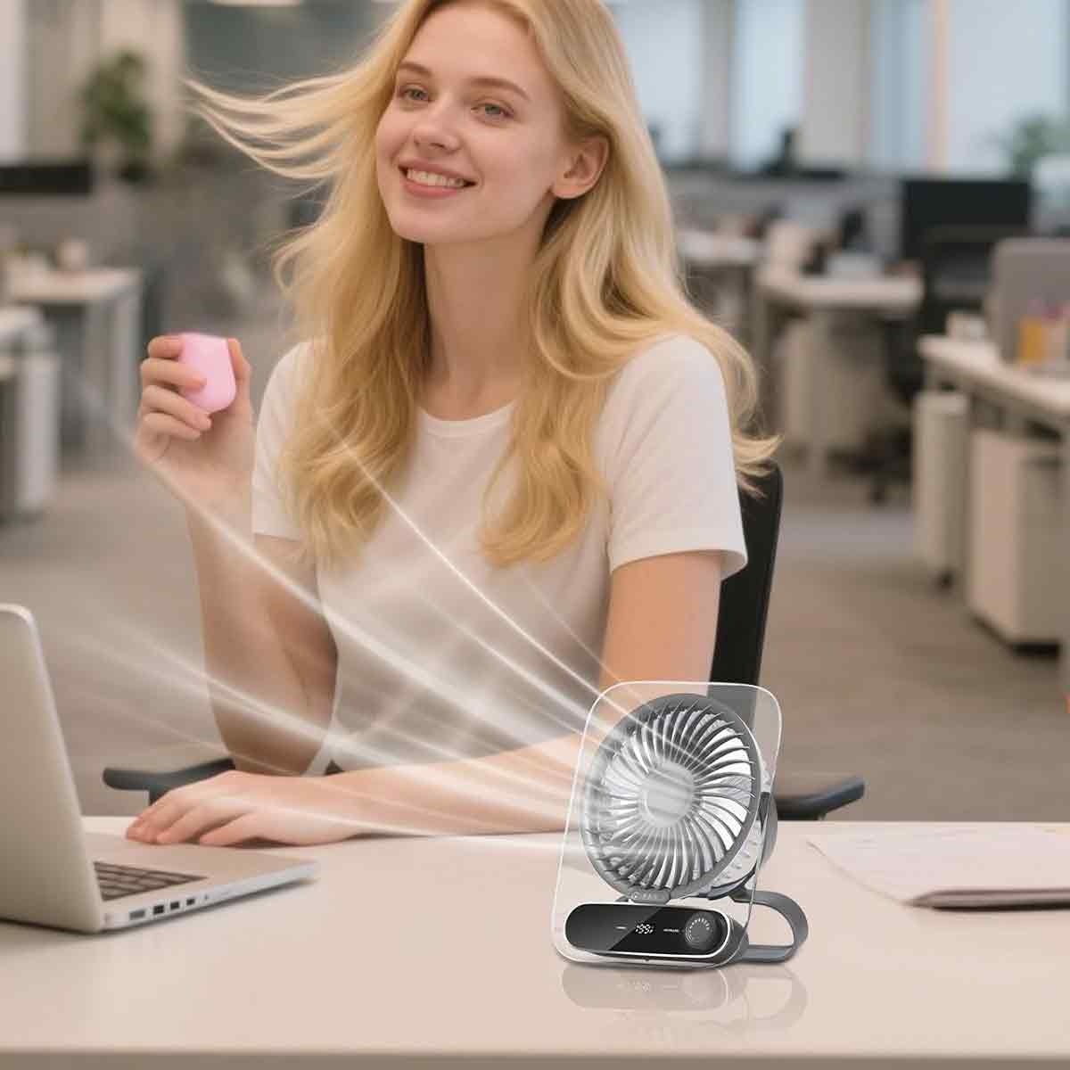 Eine Frau sitzt am Schreibtisch mit einem Laptop und einem kleinen Ventilator, der Luft bläst.