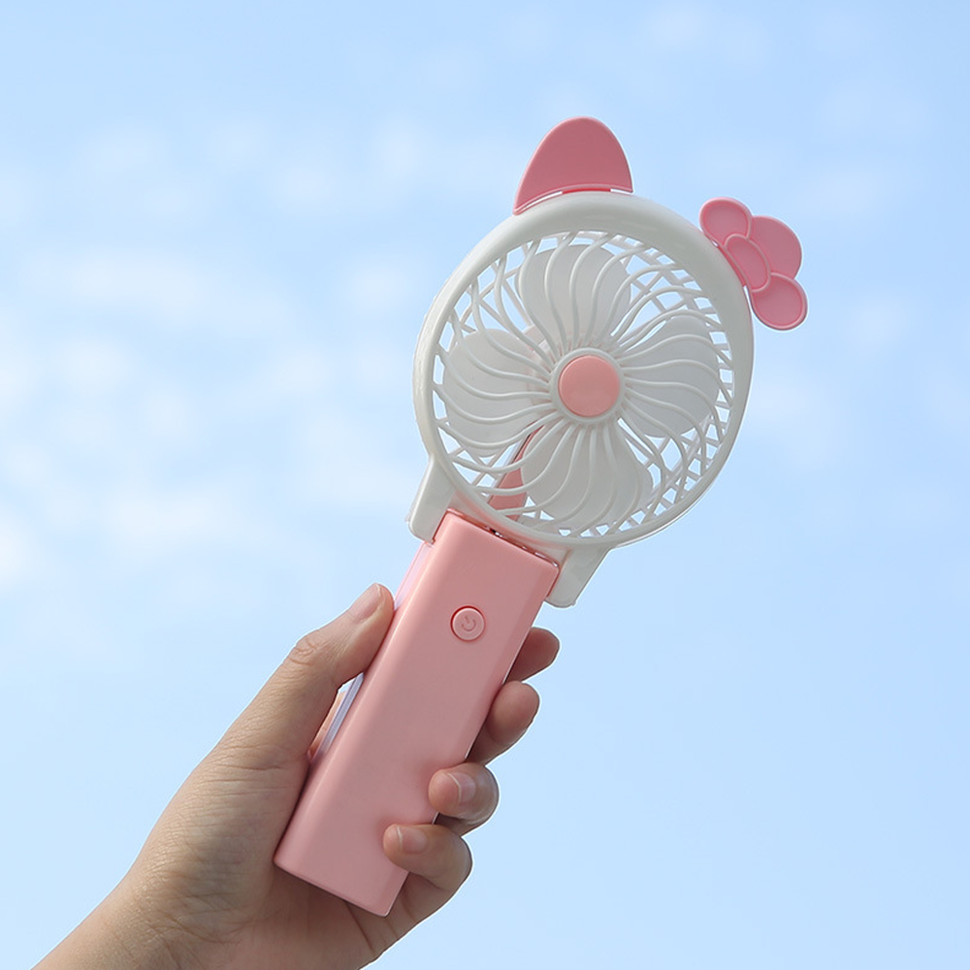 Eine Hand hält einen rosafarbenen Ventilator mit weißen Flügeln und rosa Verzierungen.