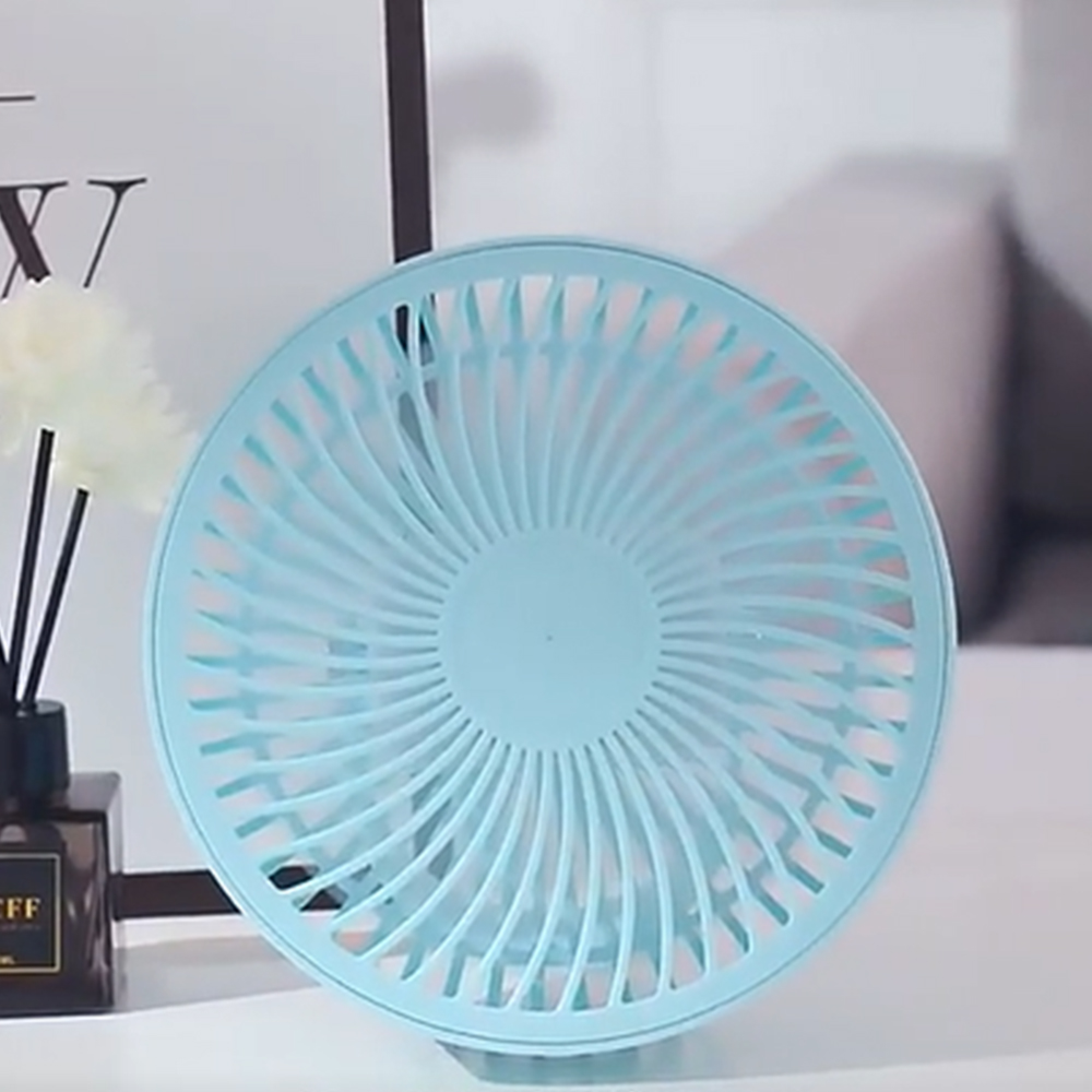 Ein hellblauer Ventilator steht auf einem Tisch mit dekorativen Gegenständen.