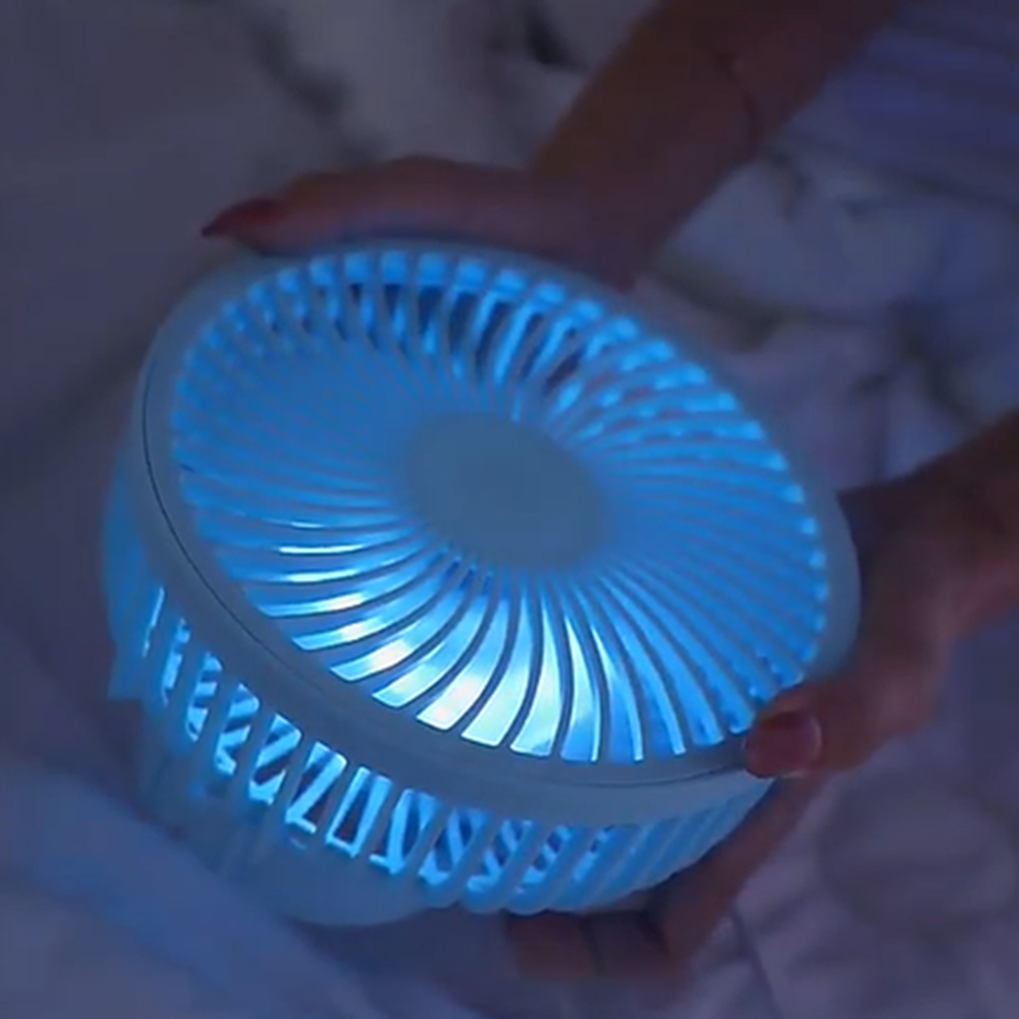 Eine Person hält einen leuchtend blauen Ventilator auf einer weißen Decke.