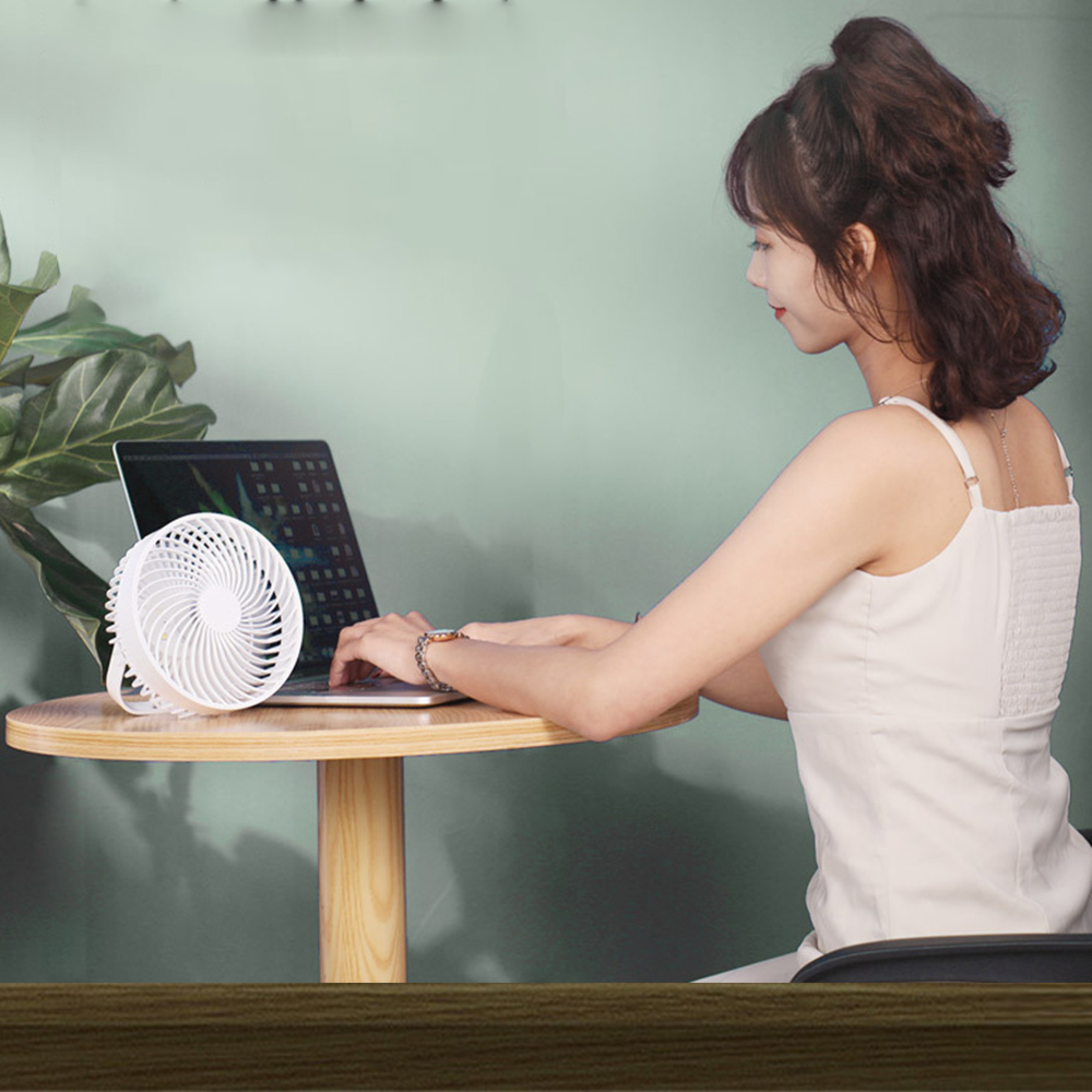 Eine Frau tippt auf einem Laptop, daneben ein kleiner weißer Ventilator.