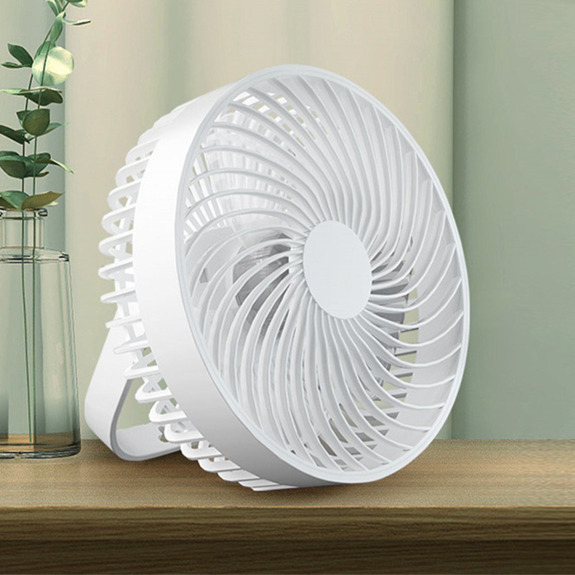 Ein weißer Ventilator steht auf einem Holztisch neben einer Glasvase mit Pflanzen.