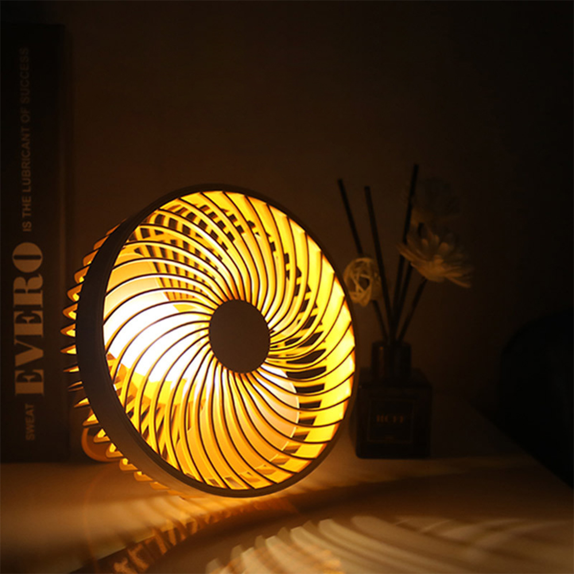 Ein beleuchteter Ventilator mit gelben Lamellen steht auf einem Tisch neben einem Buch.