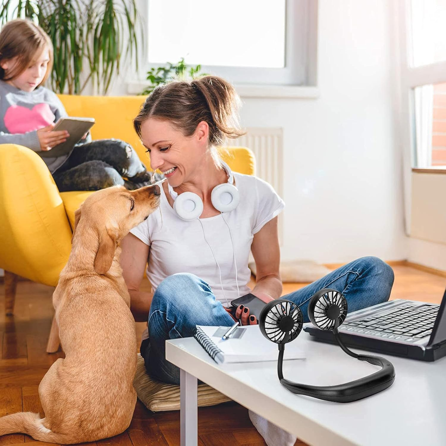 Eine Frau und ein Hund sitzen auf dem Boden. Ein Mädchen sitzt auf einem Sofa.