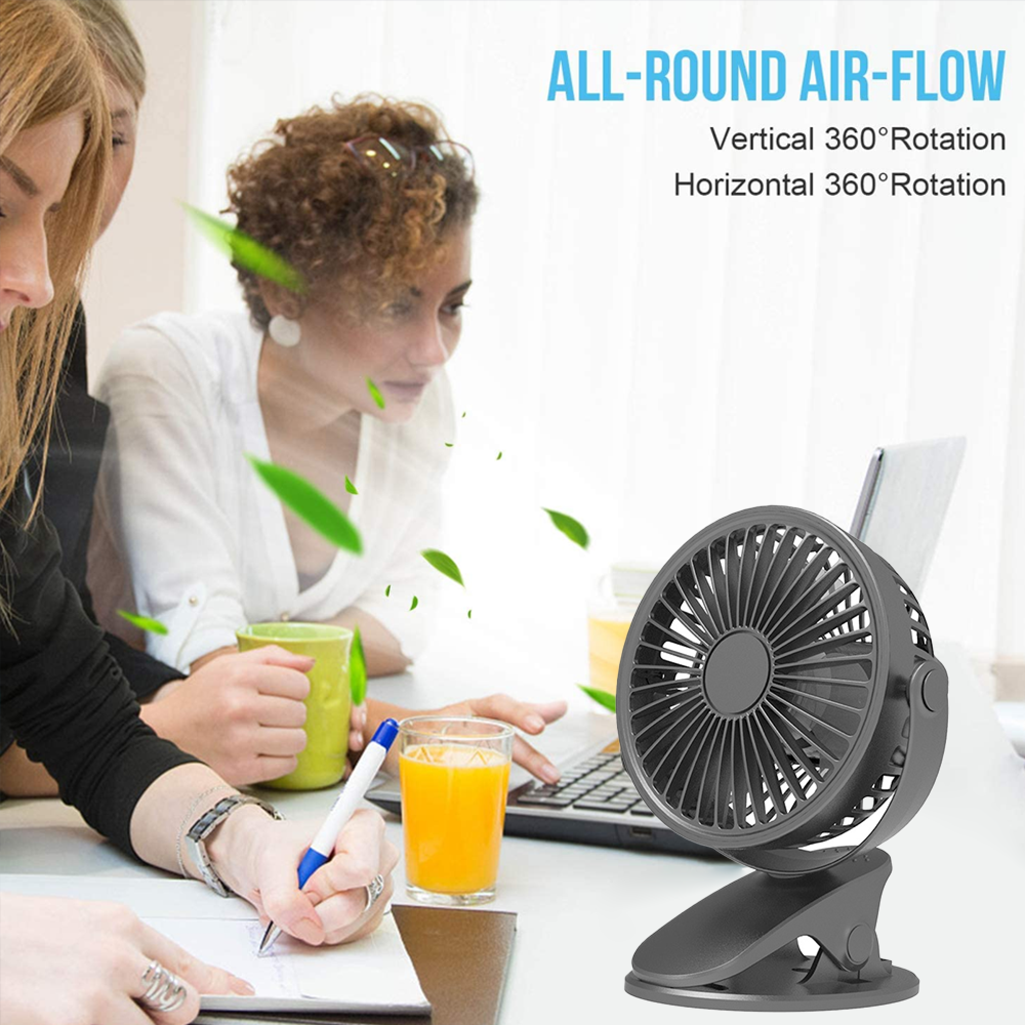 Ein kleiner schwarzer Ventilator steht auf einem Schreibtisch neben einem Laptop und Getränken.