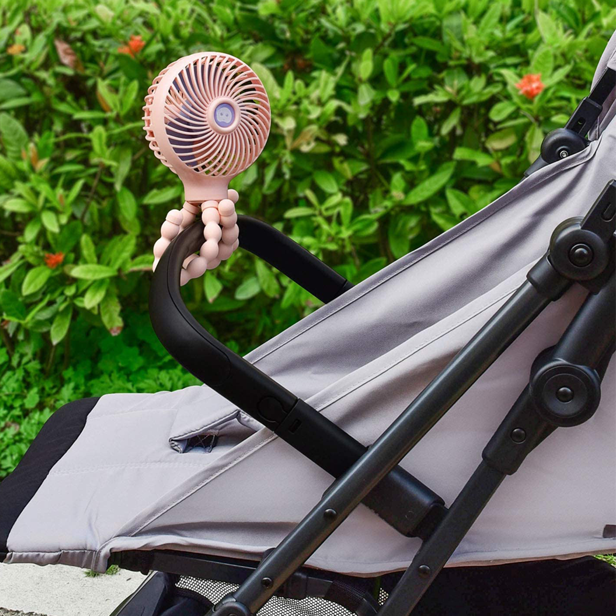 Ein rosafarbener, flexibler Ventilator ist an einem Kinderwagen befestigt.