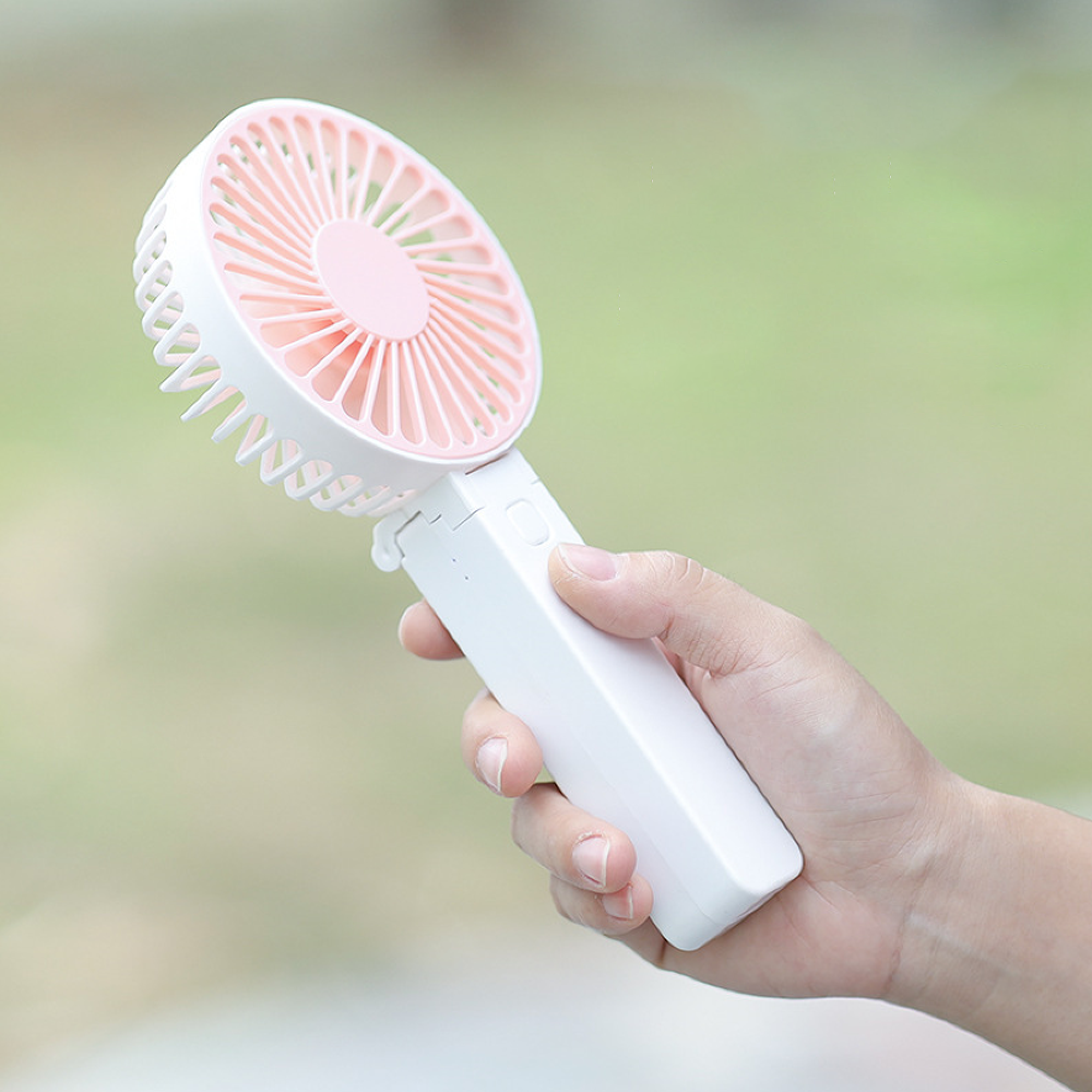 Eine Hand hält einen weißen, tragbaren Ventilator mit rosa Lüfterblättern.
