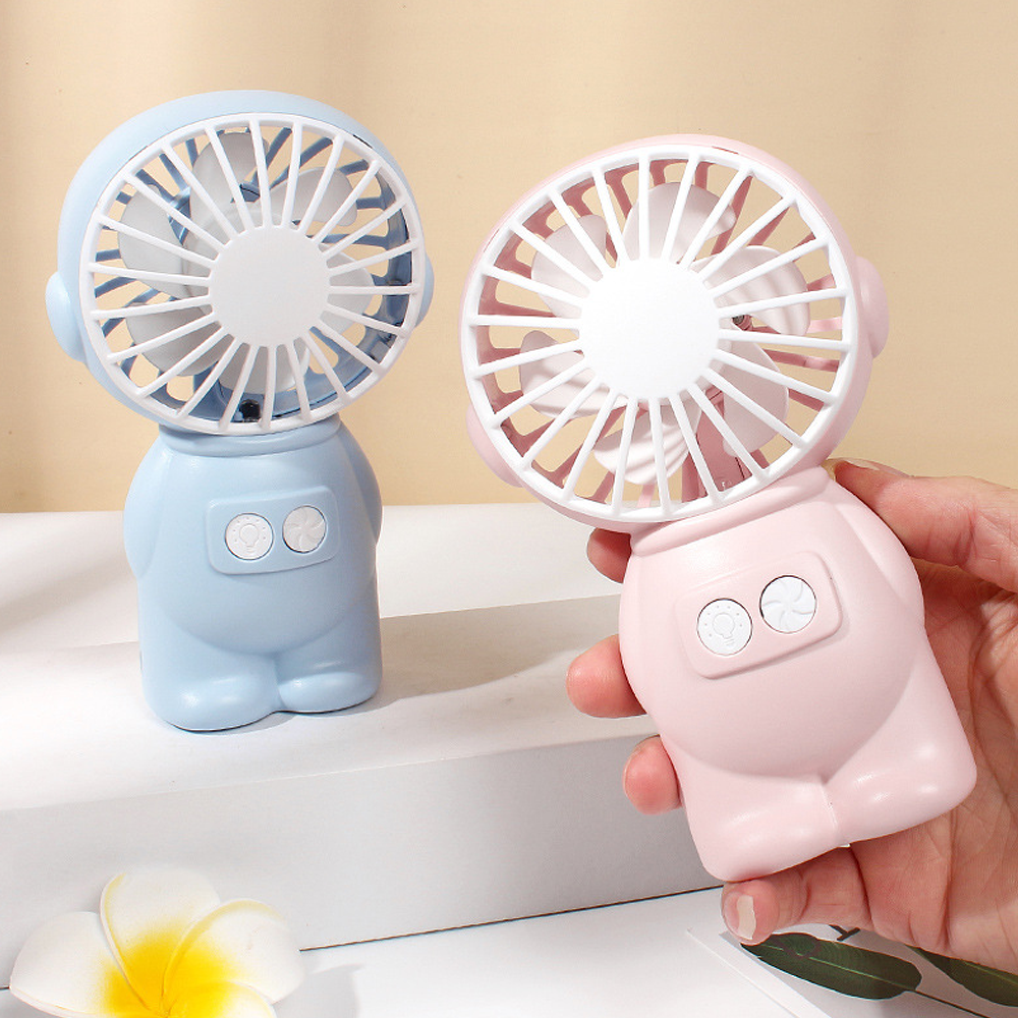 Ein blauer und ein rosa Handventilator im Astronauten-Design stehen nebeneinander.