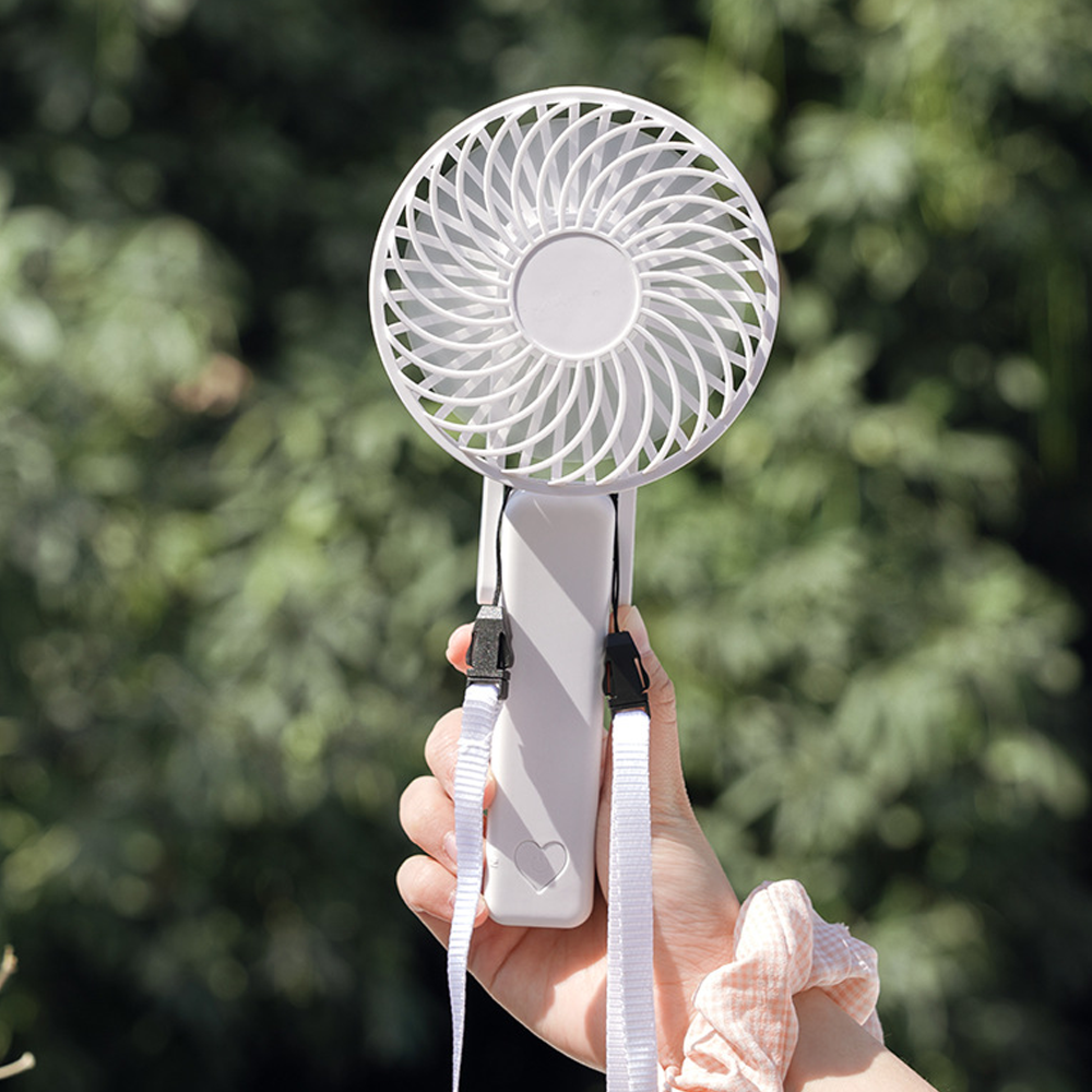 Eine Hand hält einen weißen tragbaren Ventilator mit einem Herz-Symbol auf dem Griff.