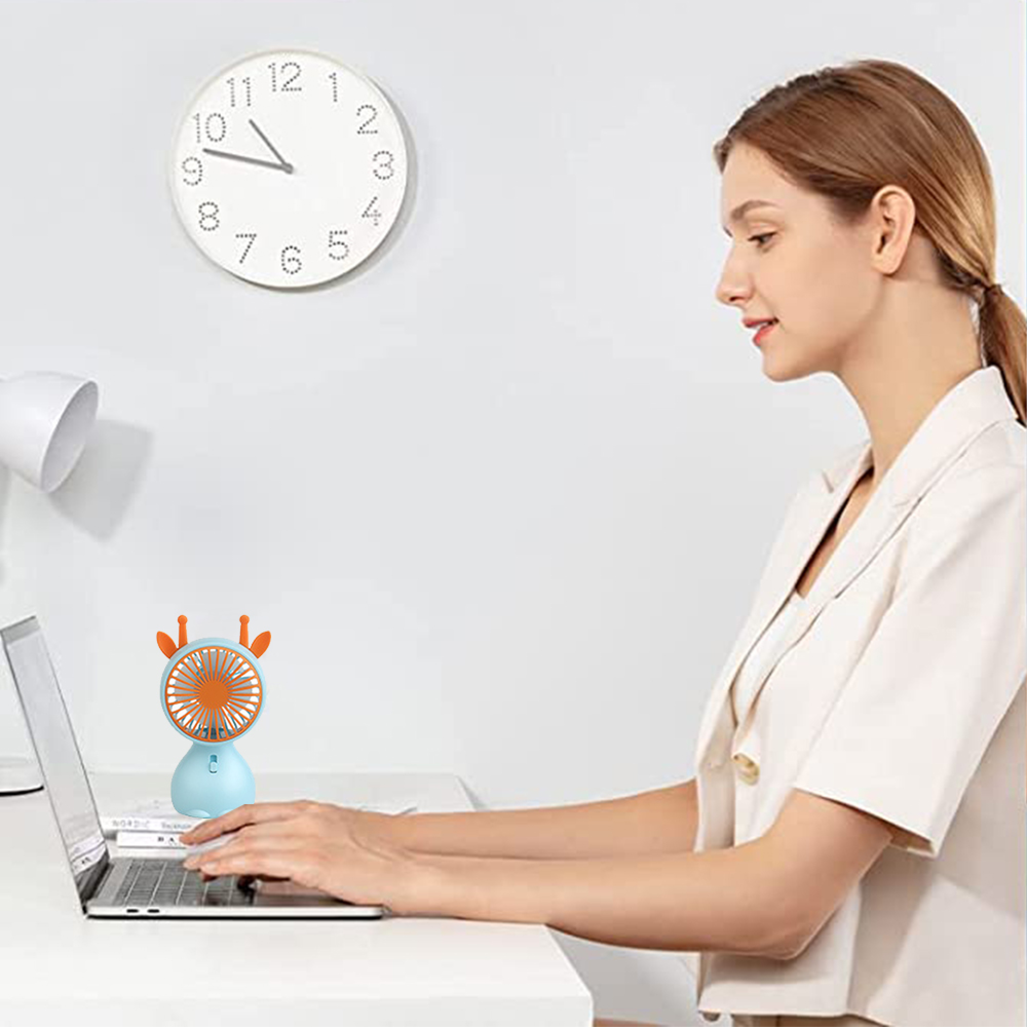 Eine Frau arbeitet an einem Laptop mit einem kleinen, blau-orangen Lüfter auf dem Schreibtisch.